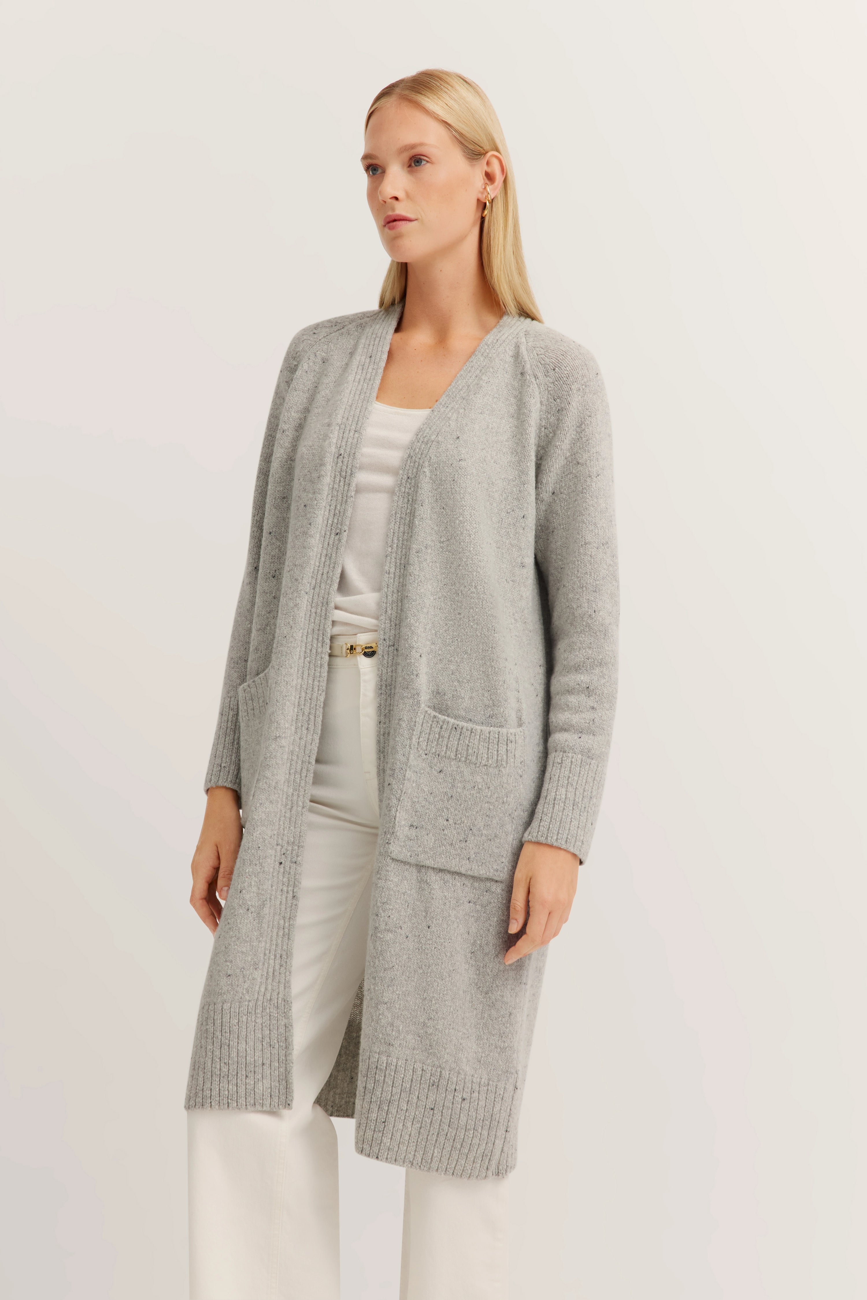 Grauer Cardigan über weißem Shirt und Hose, Model in entspannter Pose.