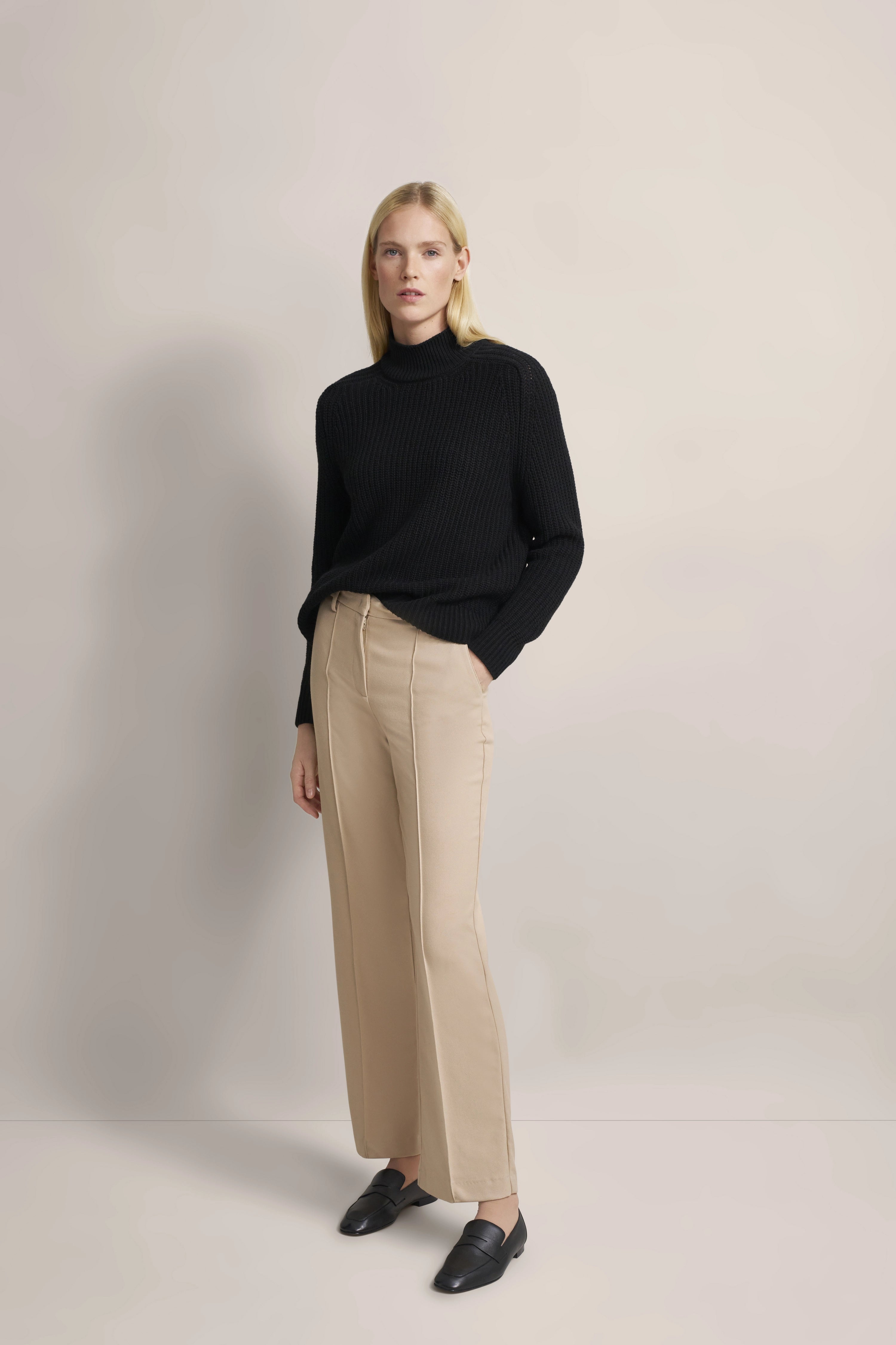 Model in schwarzem Pullover und beigen Hosen von bugatti, lässige Pose mit Händen in den Taschen.