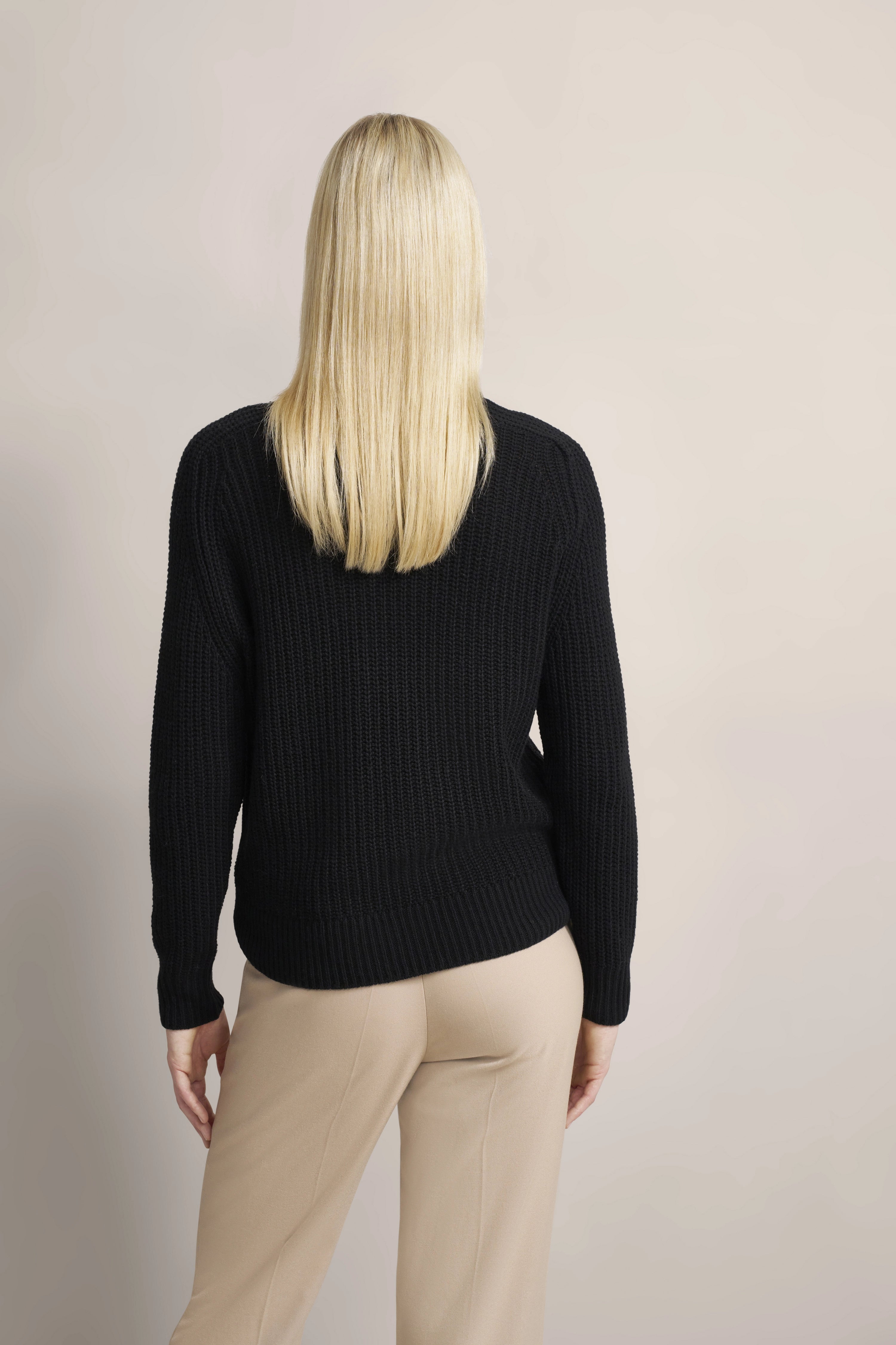 Model in schwarzem Strickpullover und beige Hose, Rückenansicht, lässige Pose.