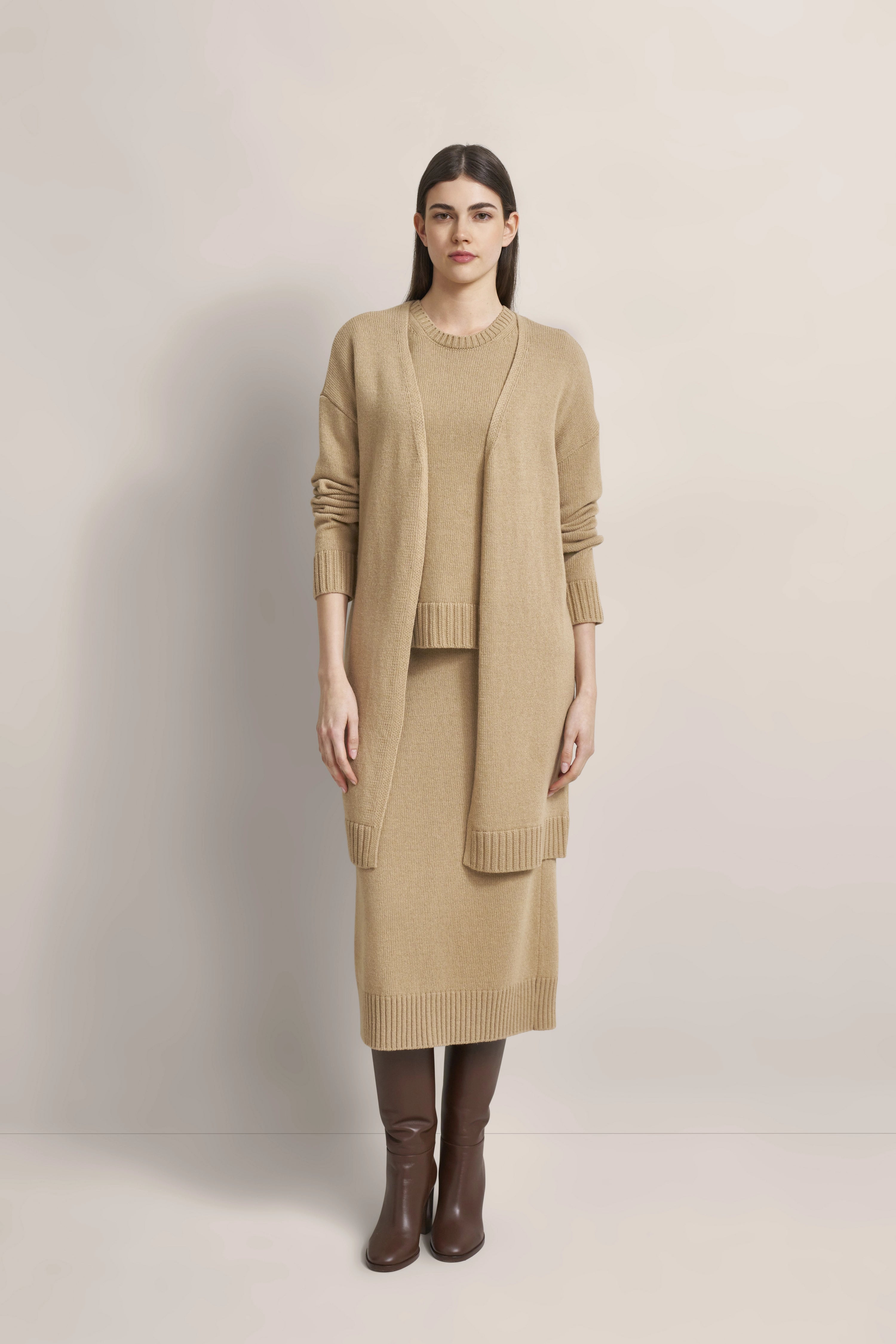 Beigefarbener Strick-Cardigan und Rock, braune Stiefel, Model steht gerade.