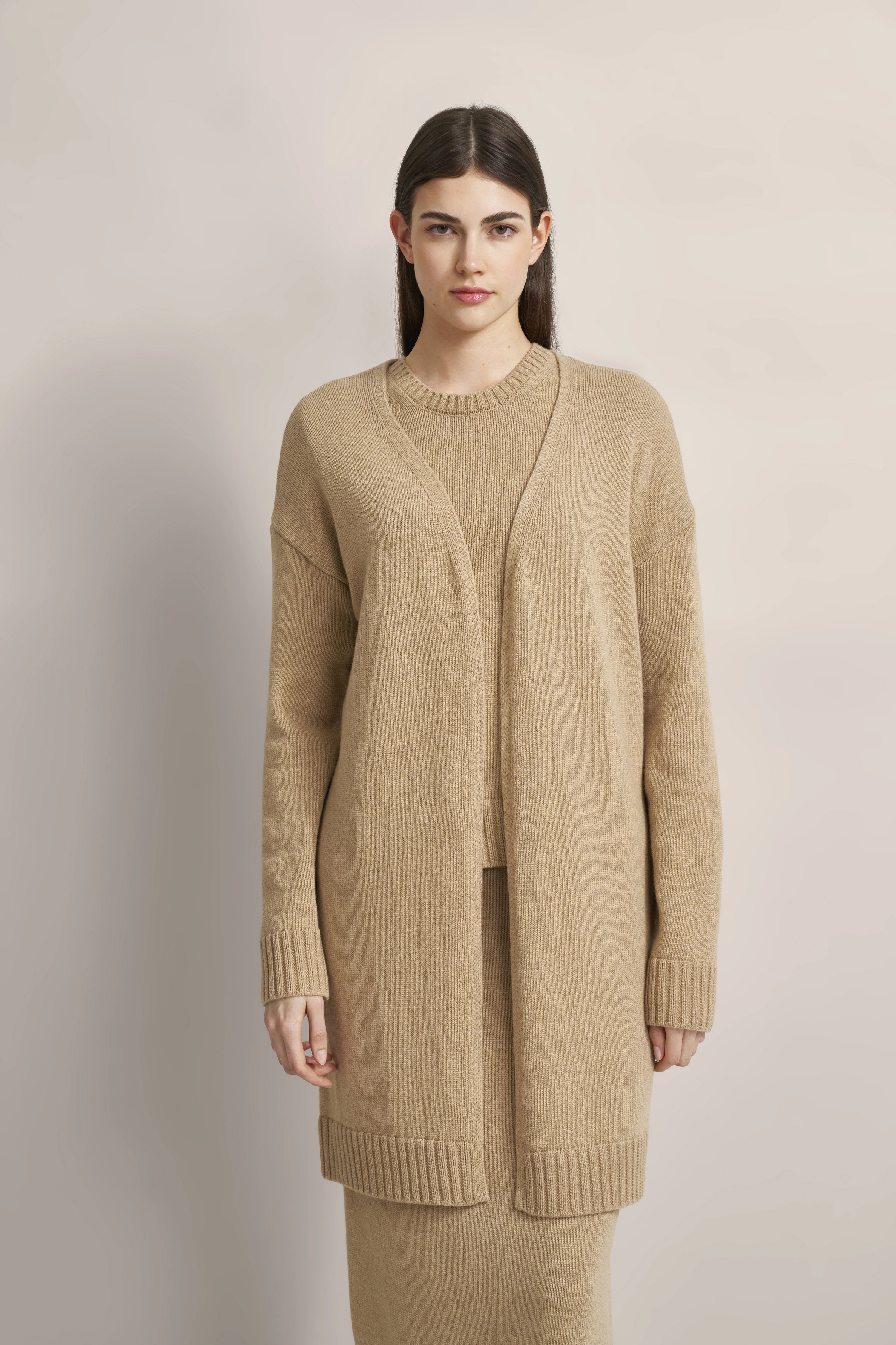 Model in beige bugatti knit set with sweater and open cardigan, standing straight.