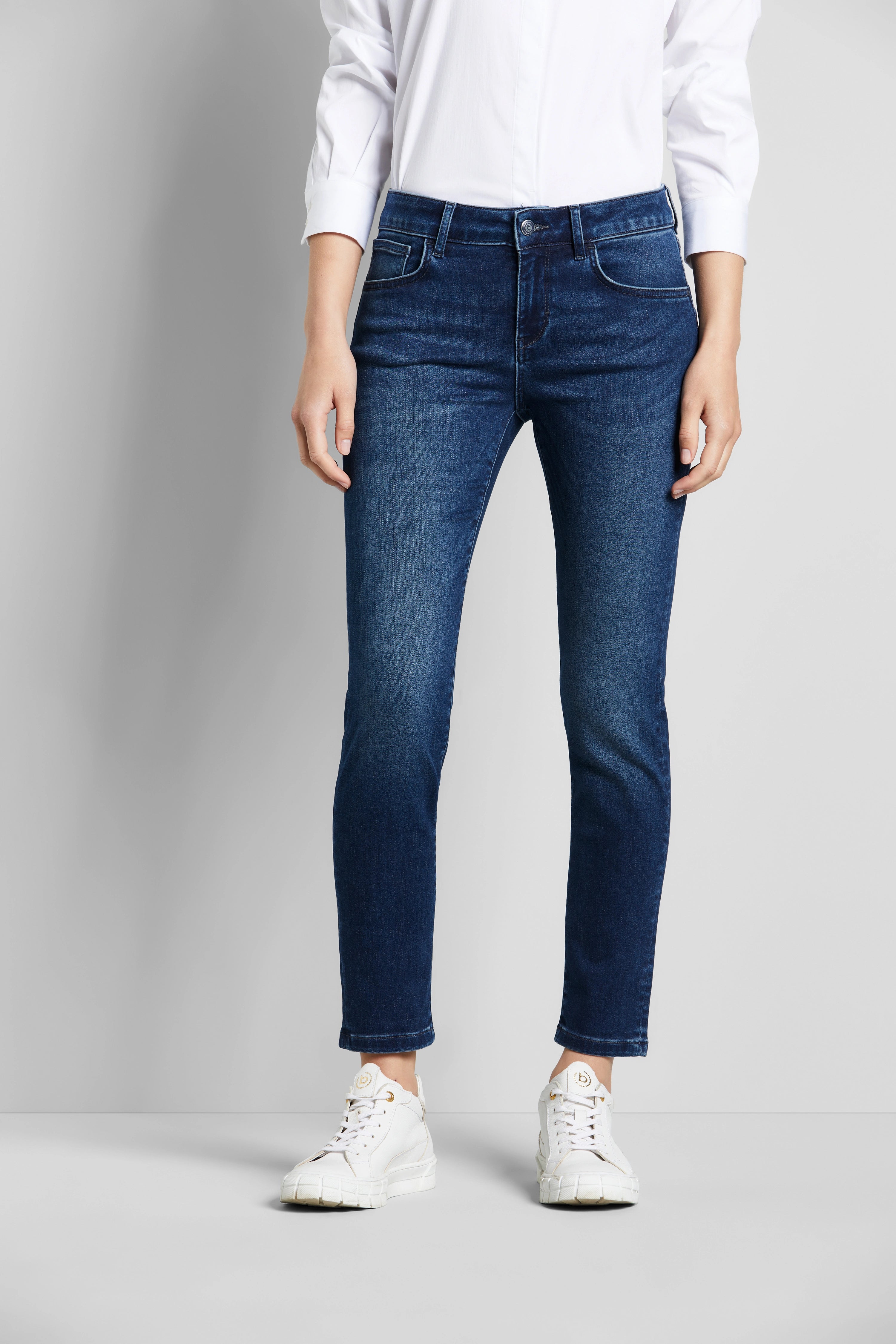bugatti weiße Bluse, blaue Jeans, weißer Sneaker, Modell zeigt lässigen Stil und italienische Eleganz.