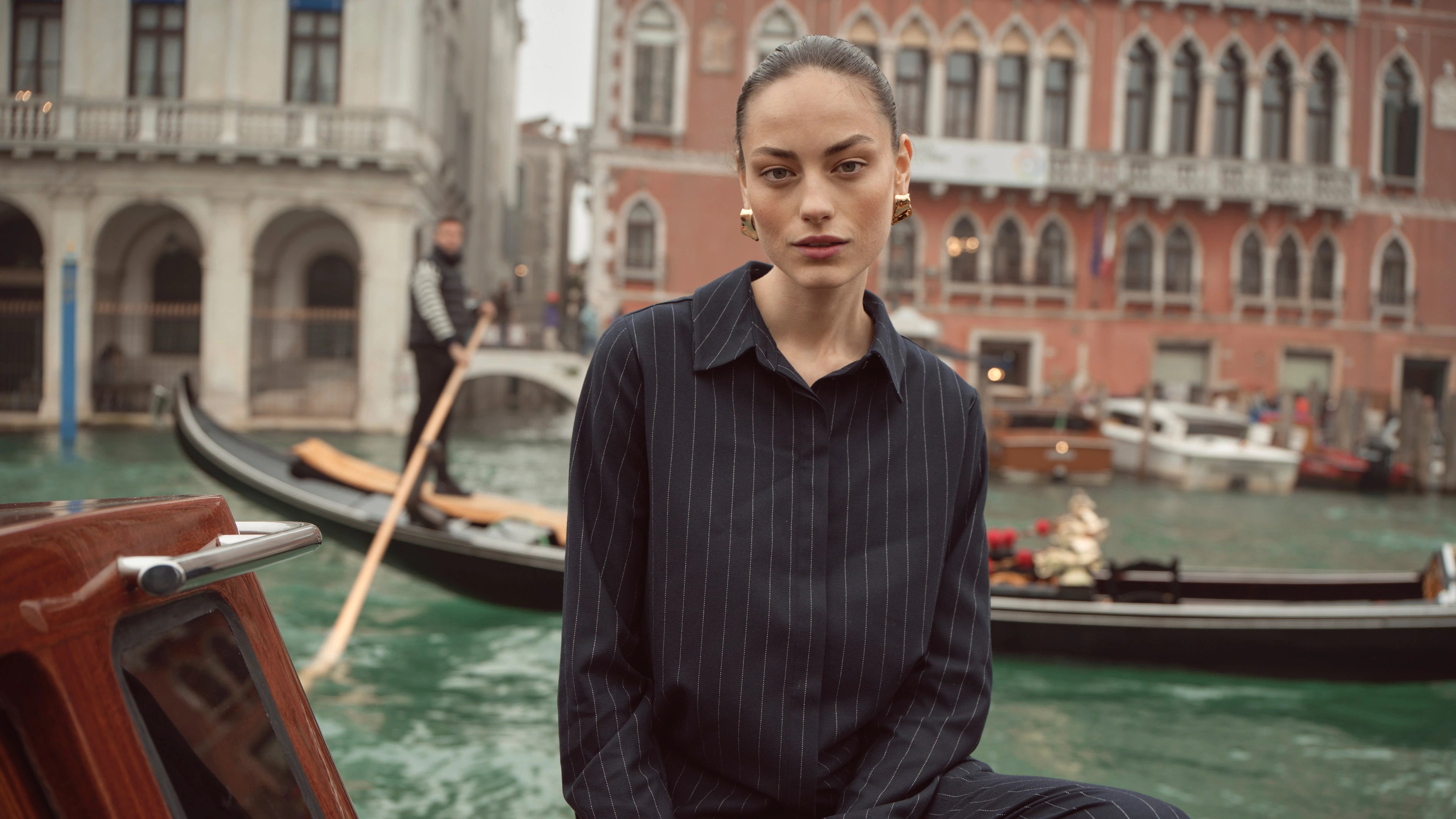 Frau trägt navyfarbenes bugatti Damenhemd mit feinen Streifen aus der Herbst/Winter-Kollektion, fotografiert vor Gondeln und Palazzi in Venedig – stilvoller Look im Venetian Chic.