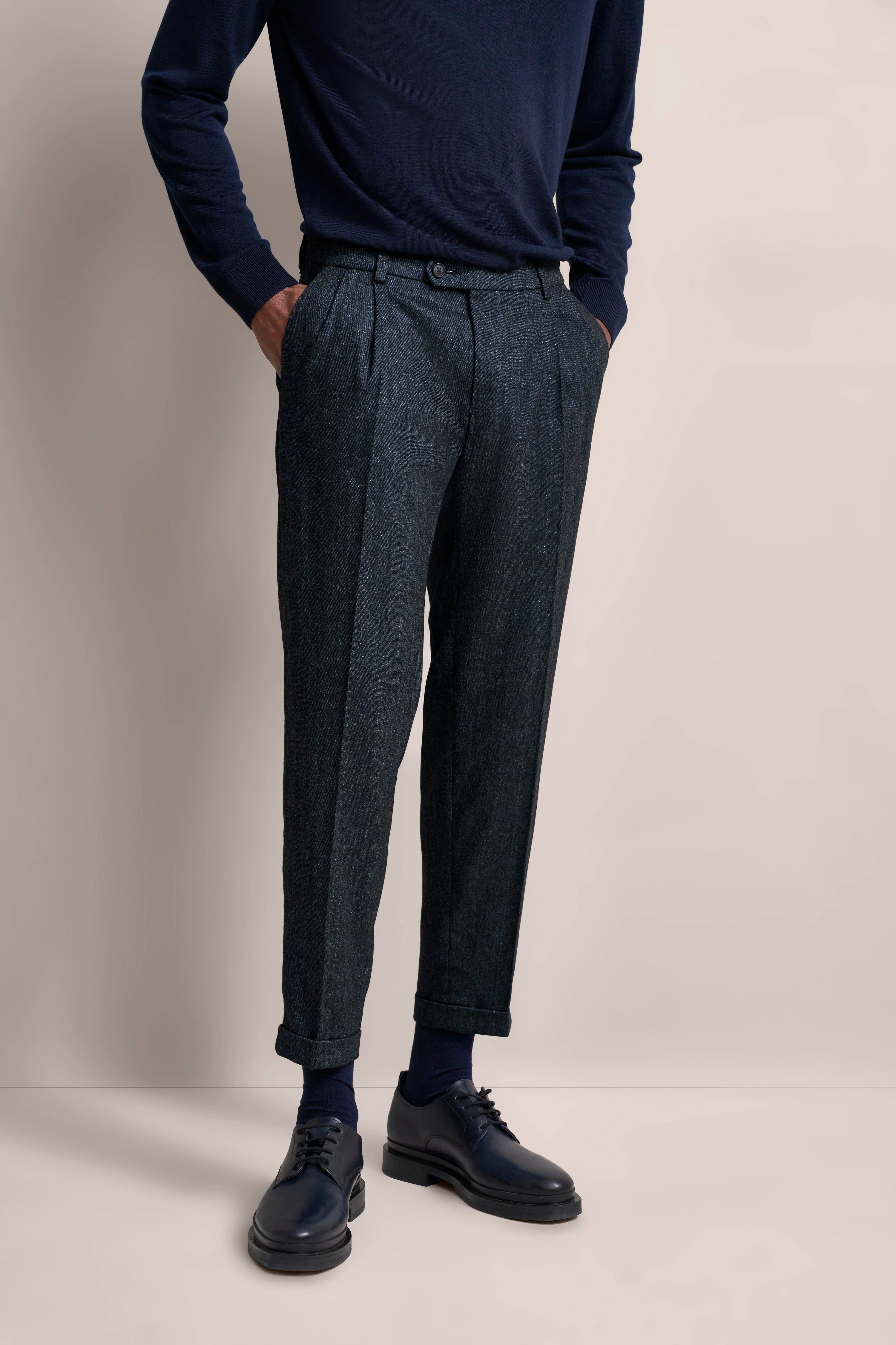 Navy Pullover und graue Anzughose, legeres Modelbild, Hände in den Hosentaschen.