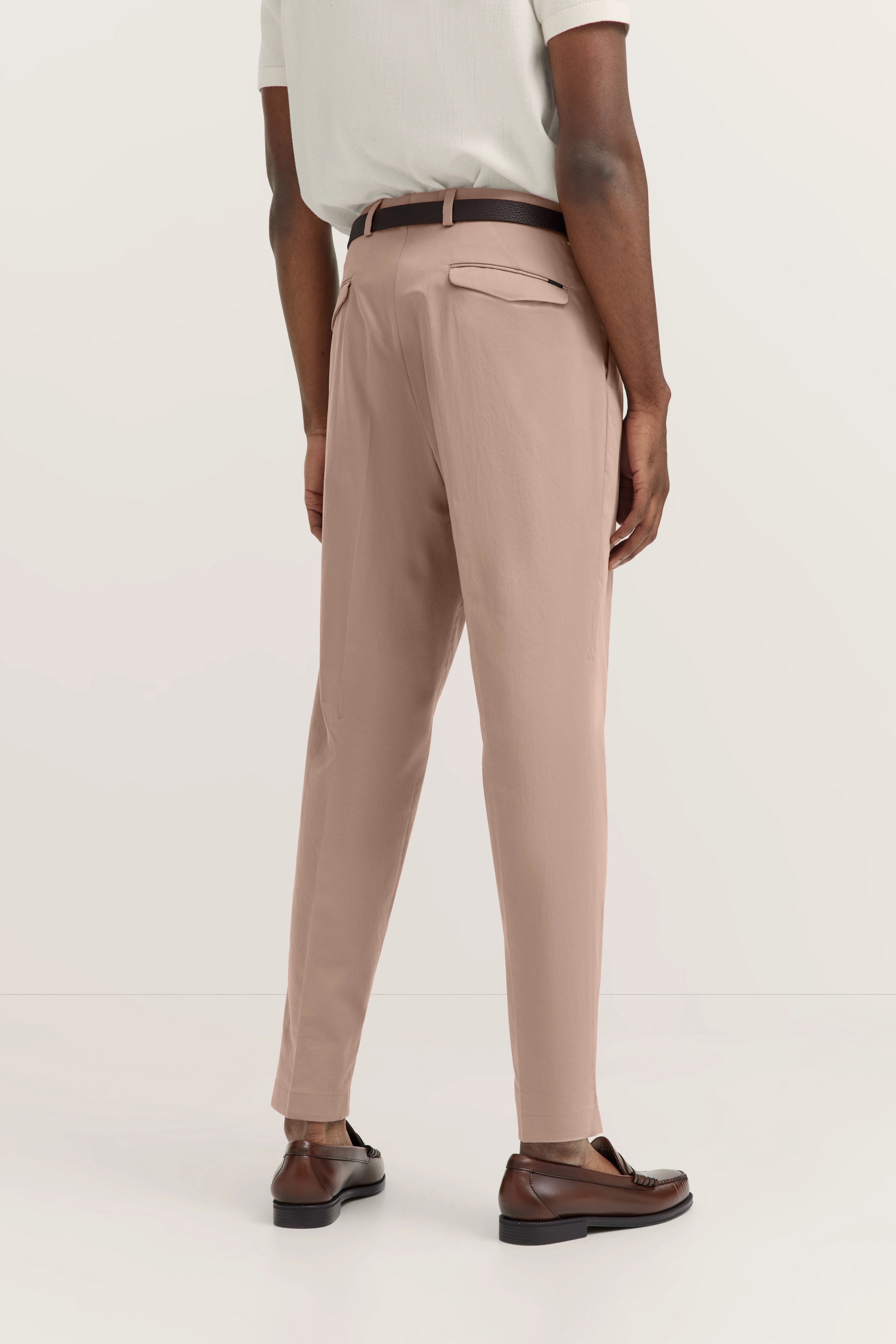 Achteraanzicht model met beige bugatti-broek, wit shirt, bruine riem en loafers, ontspannen houding.