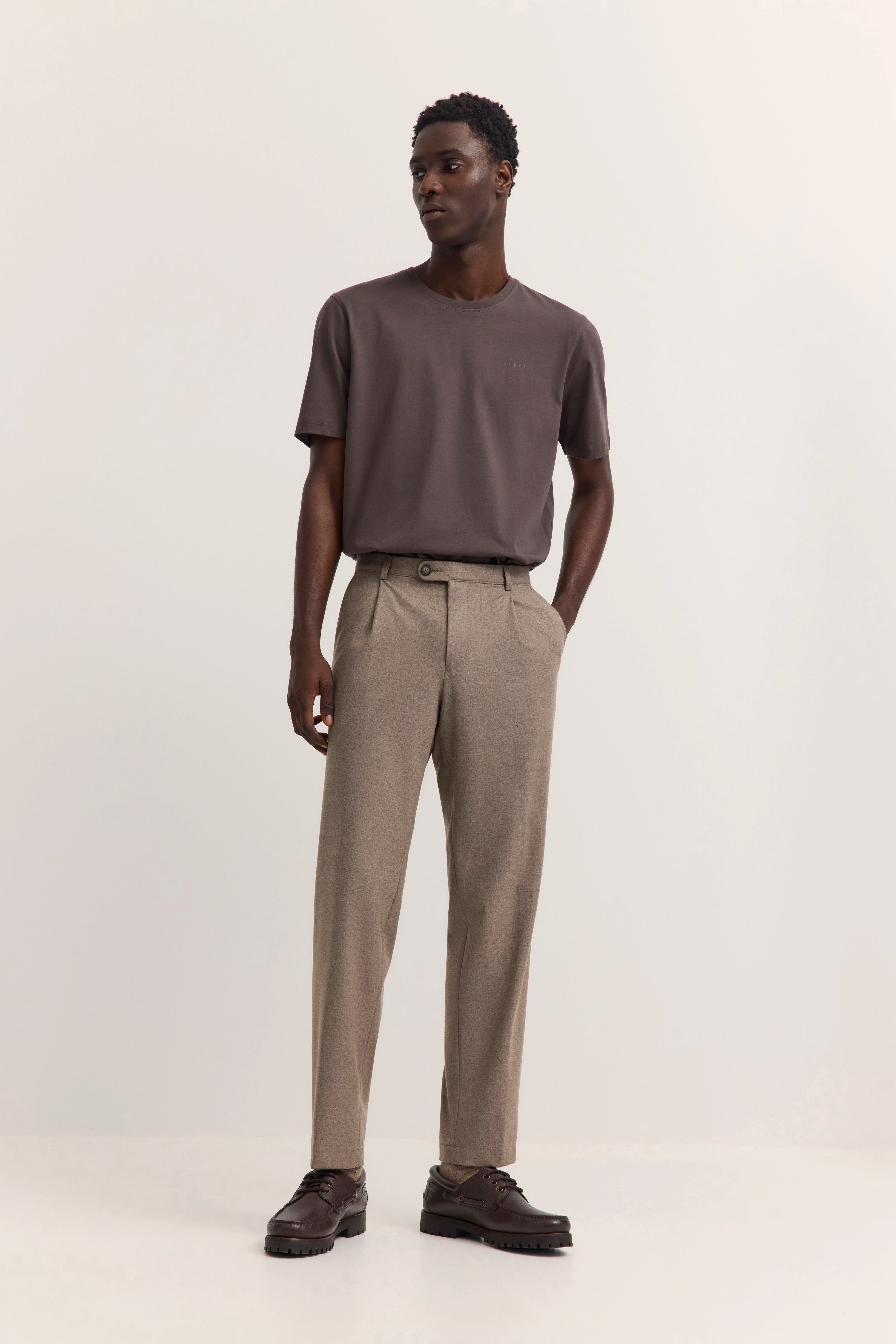 Model im legeren Outfit: braunes T-Shirt, beige Hose, braune Schuhe. Lockeres, entspanntes Posing.