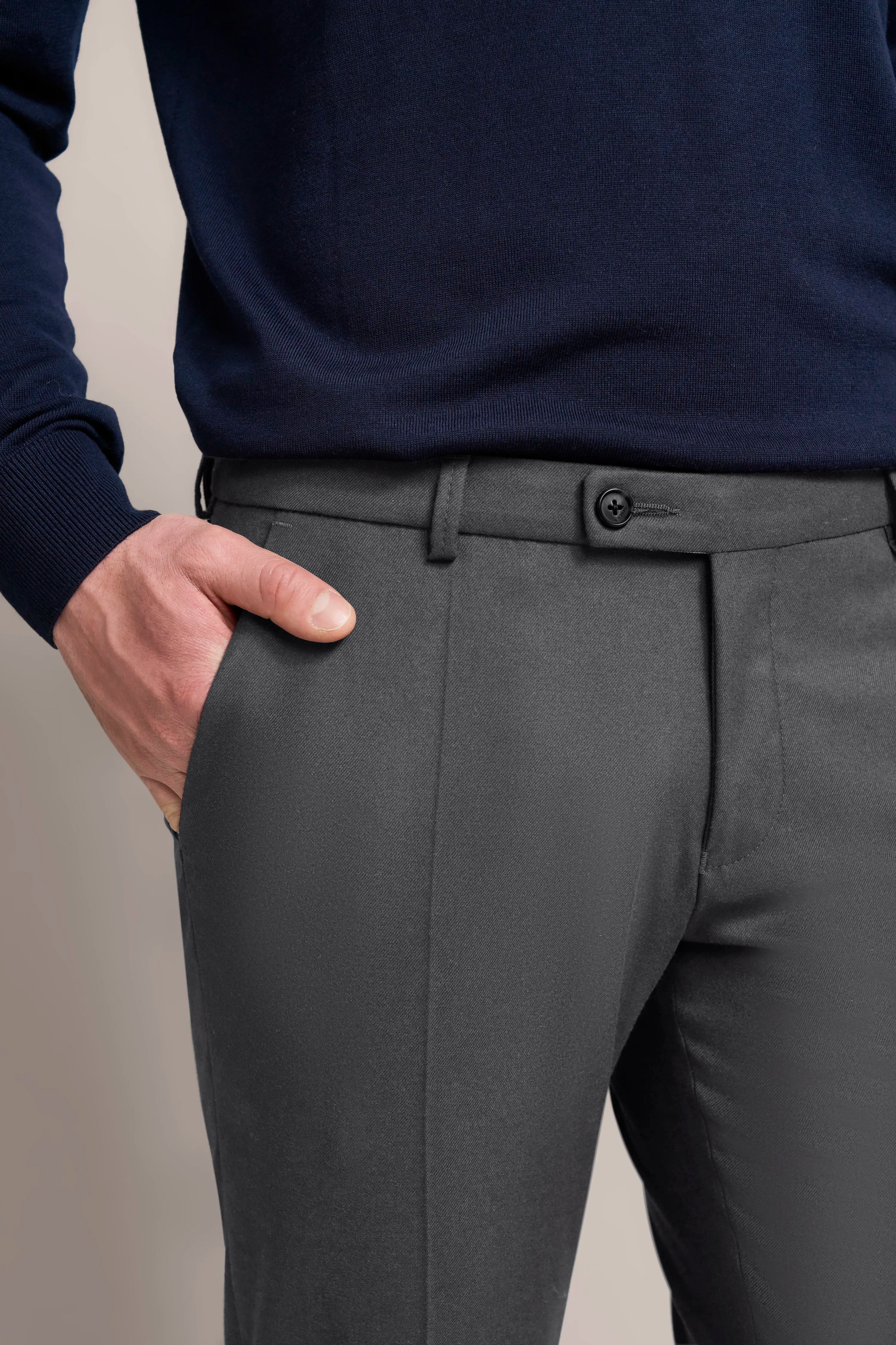 Navy sweater and grey trousers, casual bust shot with hand in pocket.
