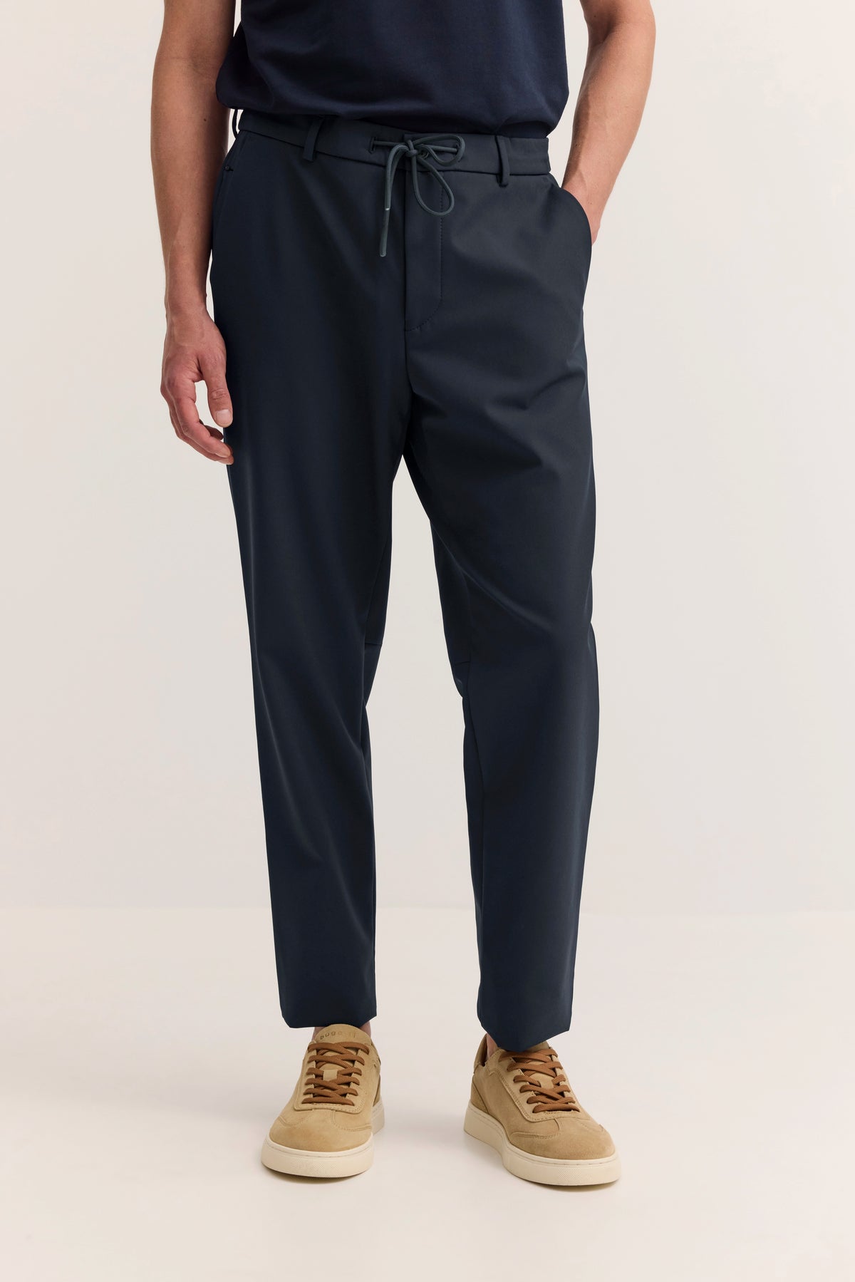 Dunkelblaue bugatti-Hose, legeres Modelbild, Hände in Taschen, mit beigen Sneakers.