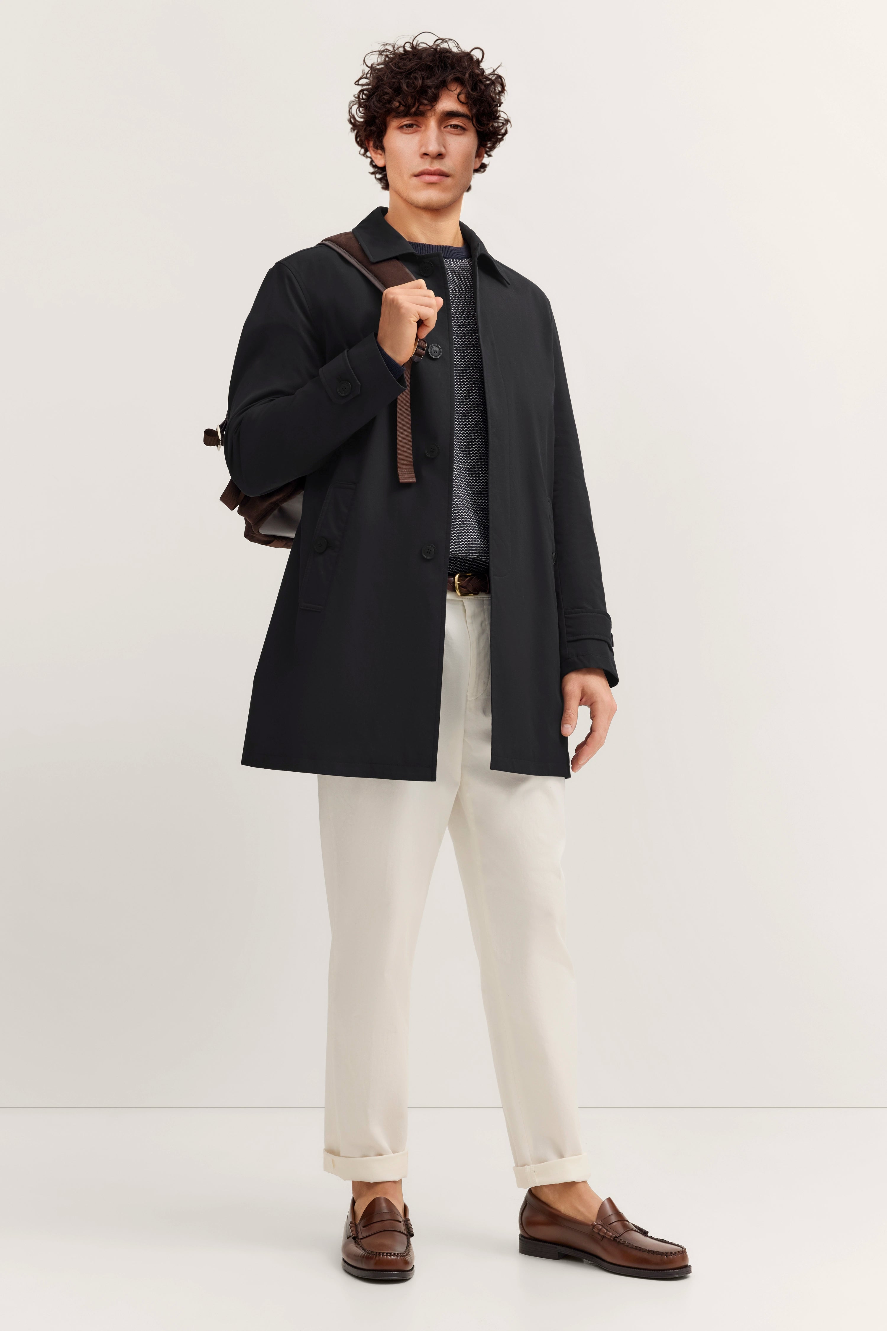 Model in schwarzem bugatti Mantel, Rückenansicht, legeres Posing, weiße Hose.
