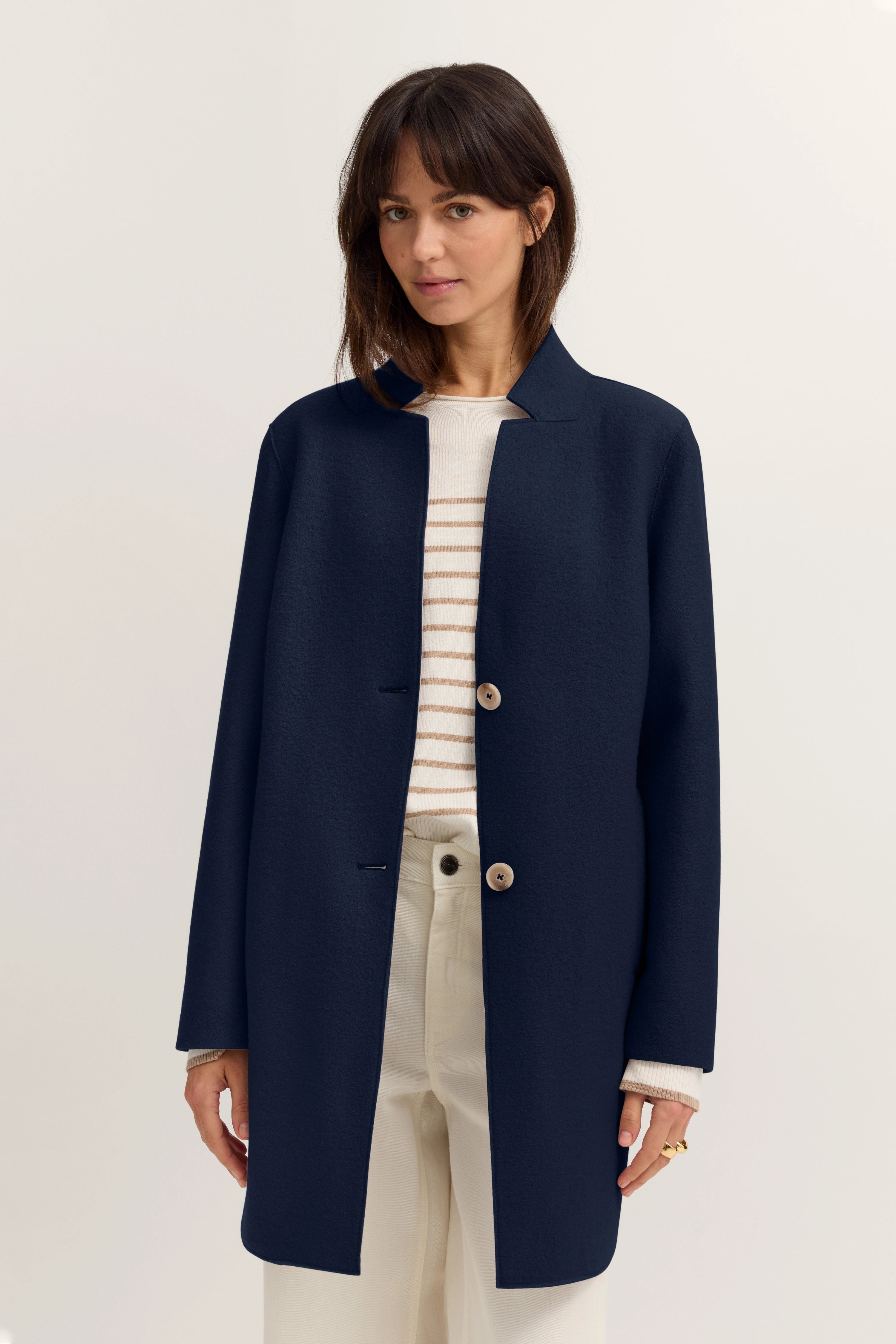 Navyblauer bugatti Mantel, gestreifter Pullover, cremefarbene Hose, Modelbild, entspannte Haltung.