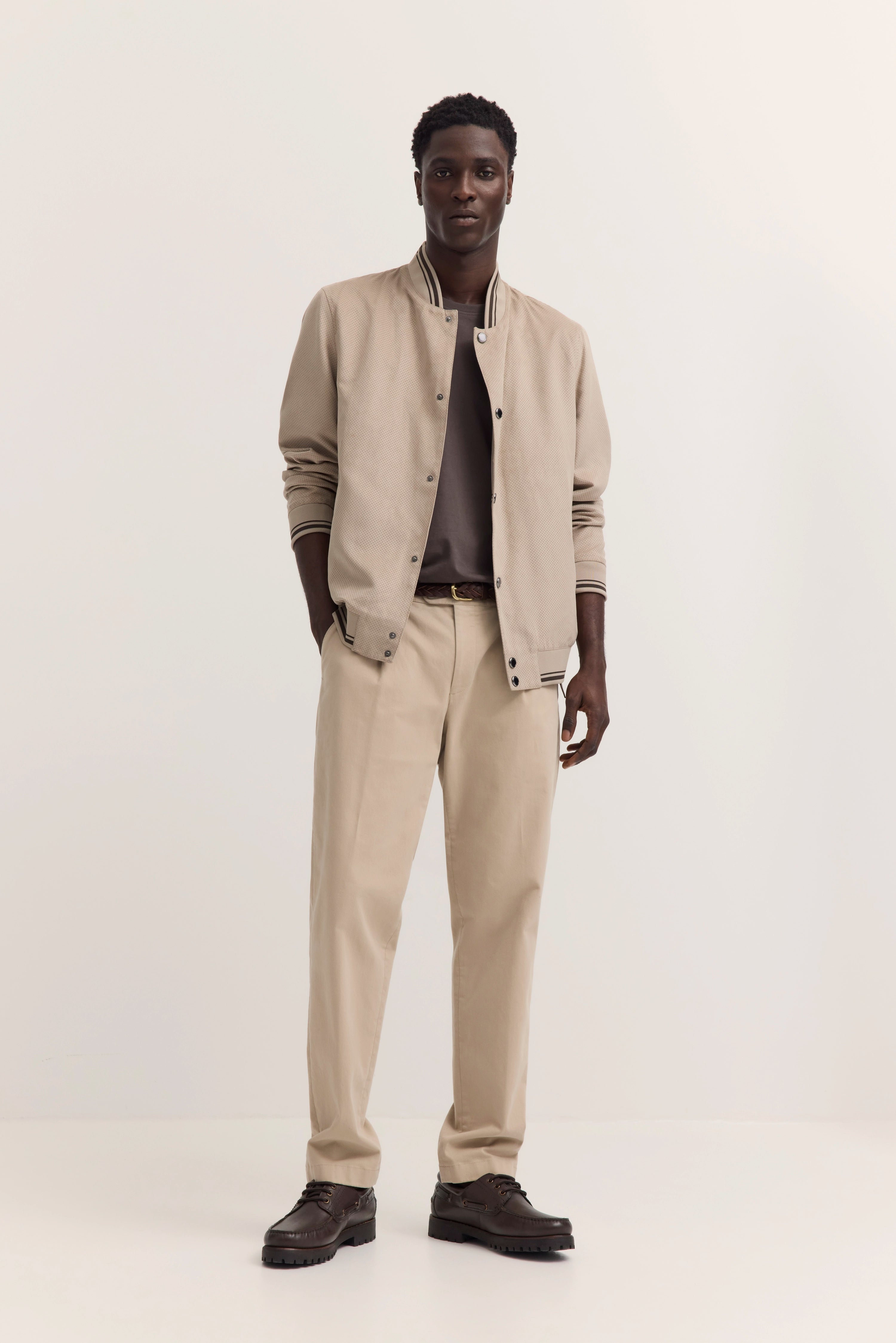 Beiges bugatti Outfit mit Jacke, T-Shirt und Hose, Model posiert stehend, lässig-elegant.