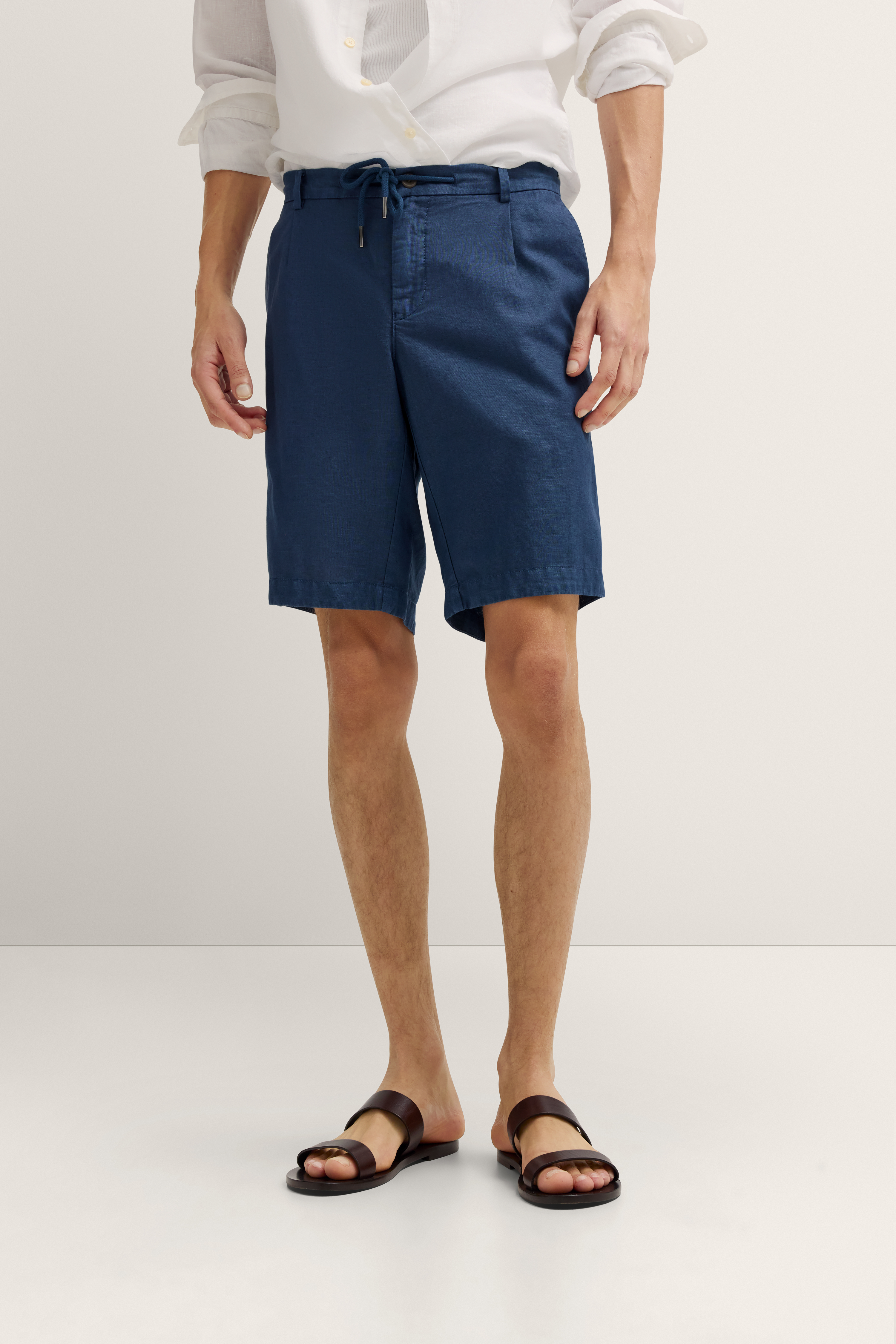 bugatti Modelbild: Weißes Hemd, blaue Shorts, braune Sandalen, lässige Pose.