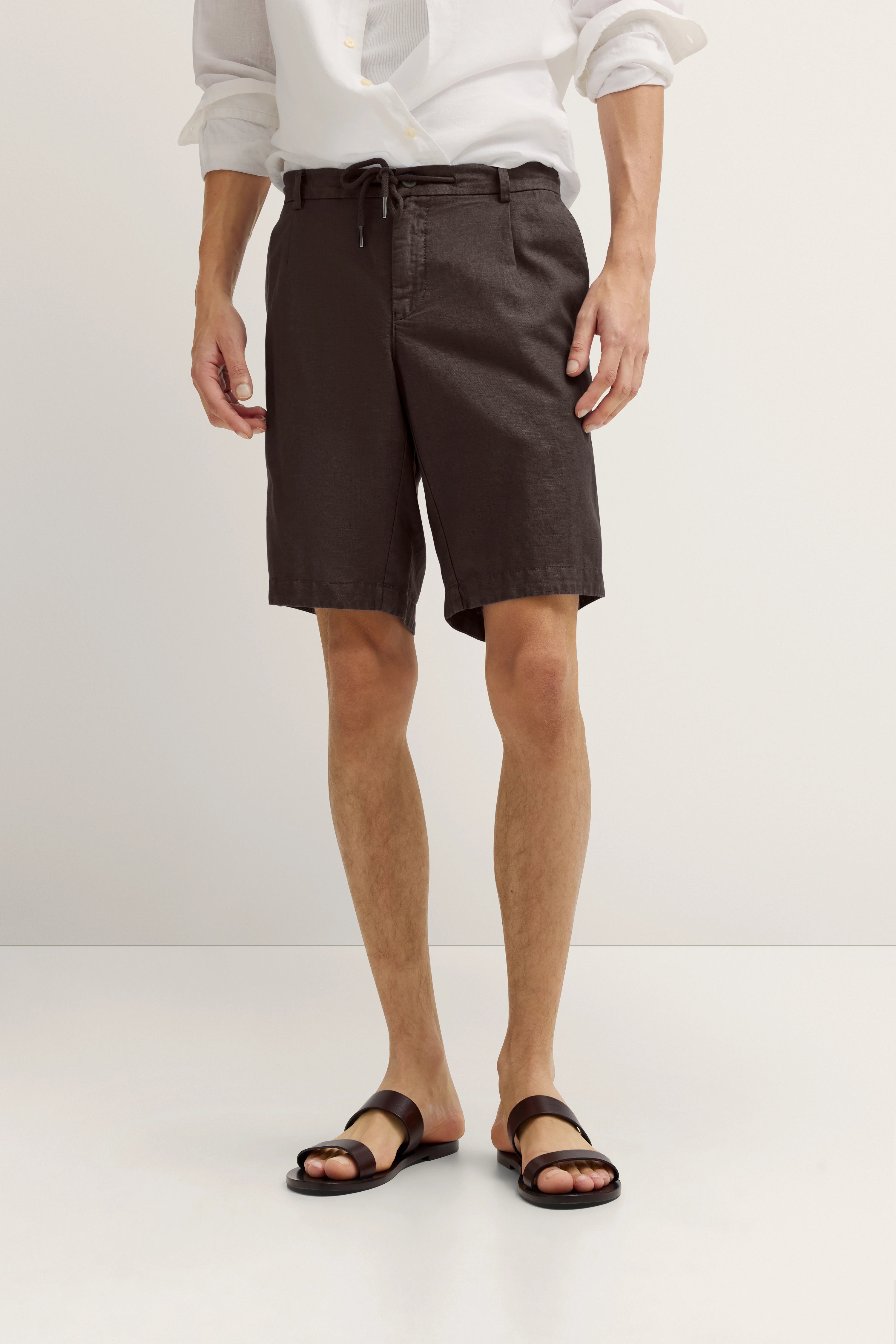 Weiße Hemd und braune Shorts Outfit, legeres Modelbild, entspannte Pose.