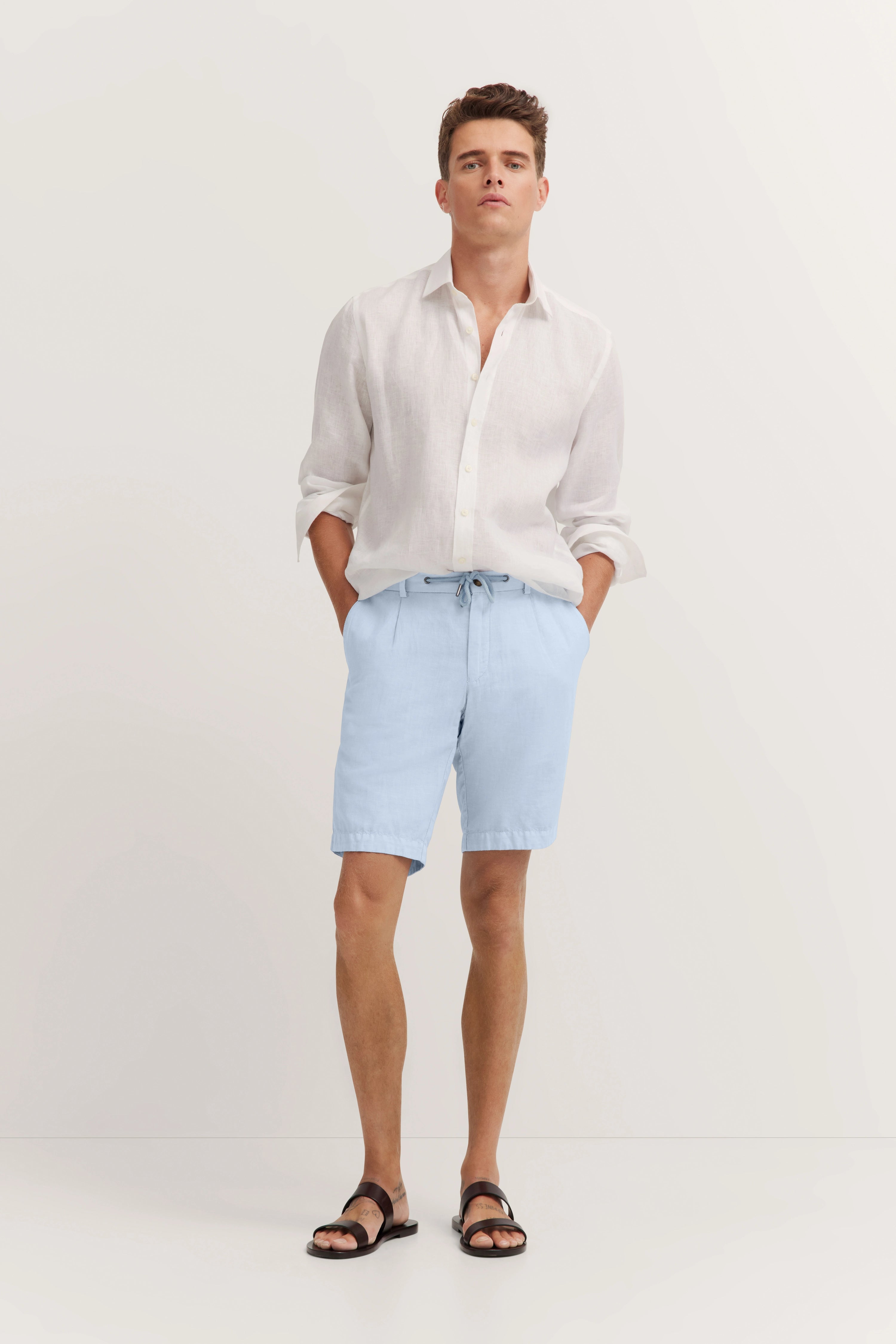 Helles Leinenhemd und blaue Shorts, legeres Modelbild von hinten, entspannte Pose.