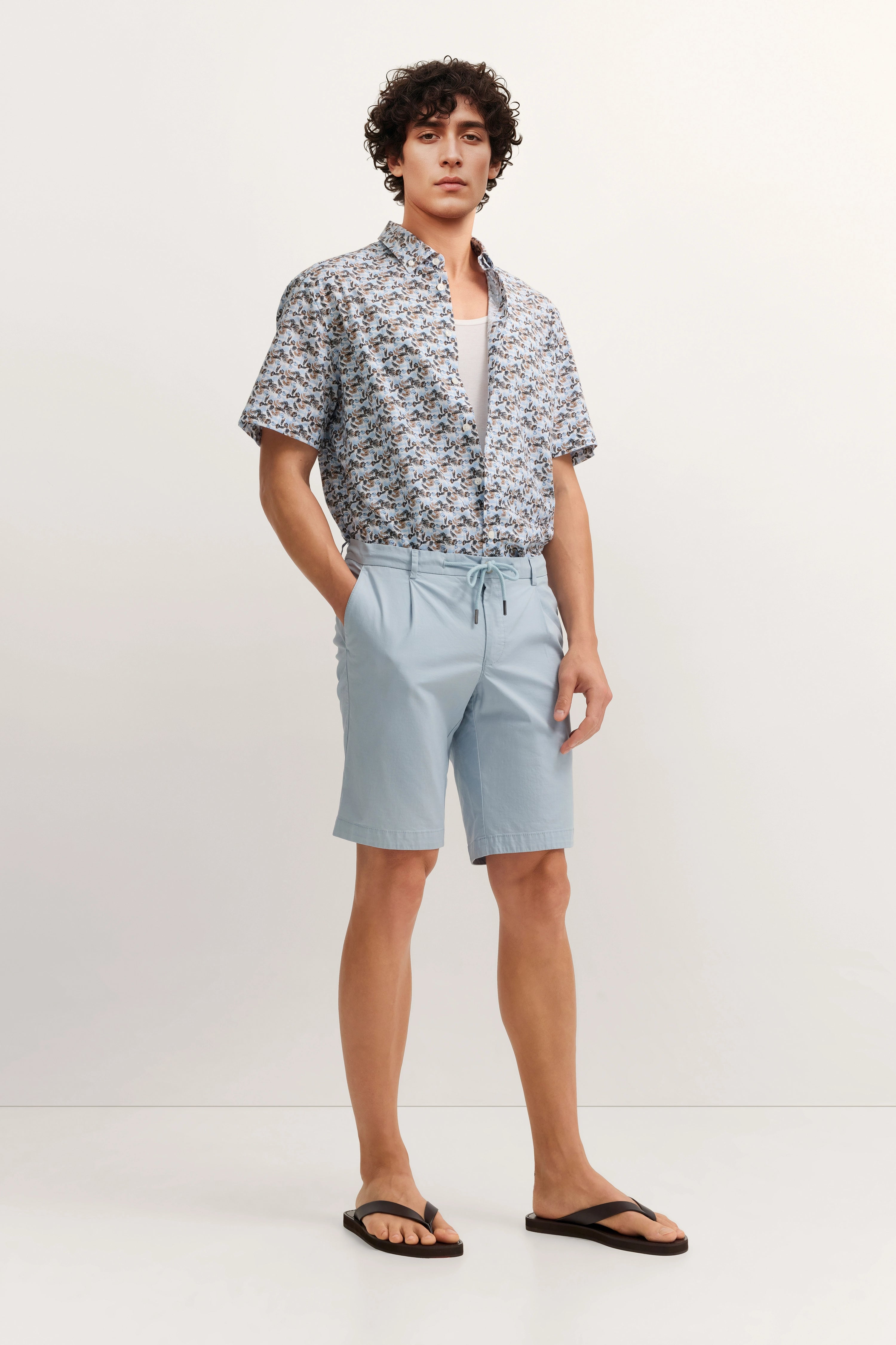 Model in gemustertem bugatti-Hemd und hellblauen Shorts, lässig stehend.