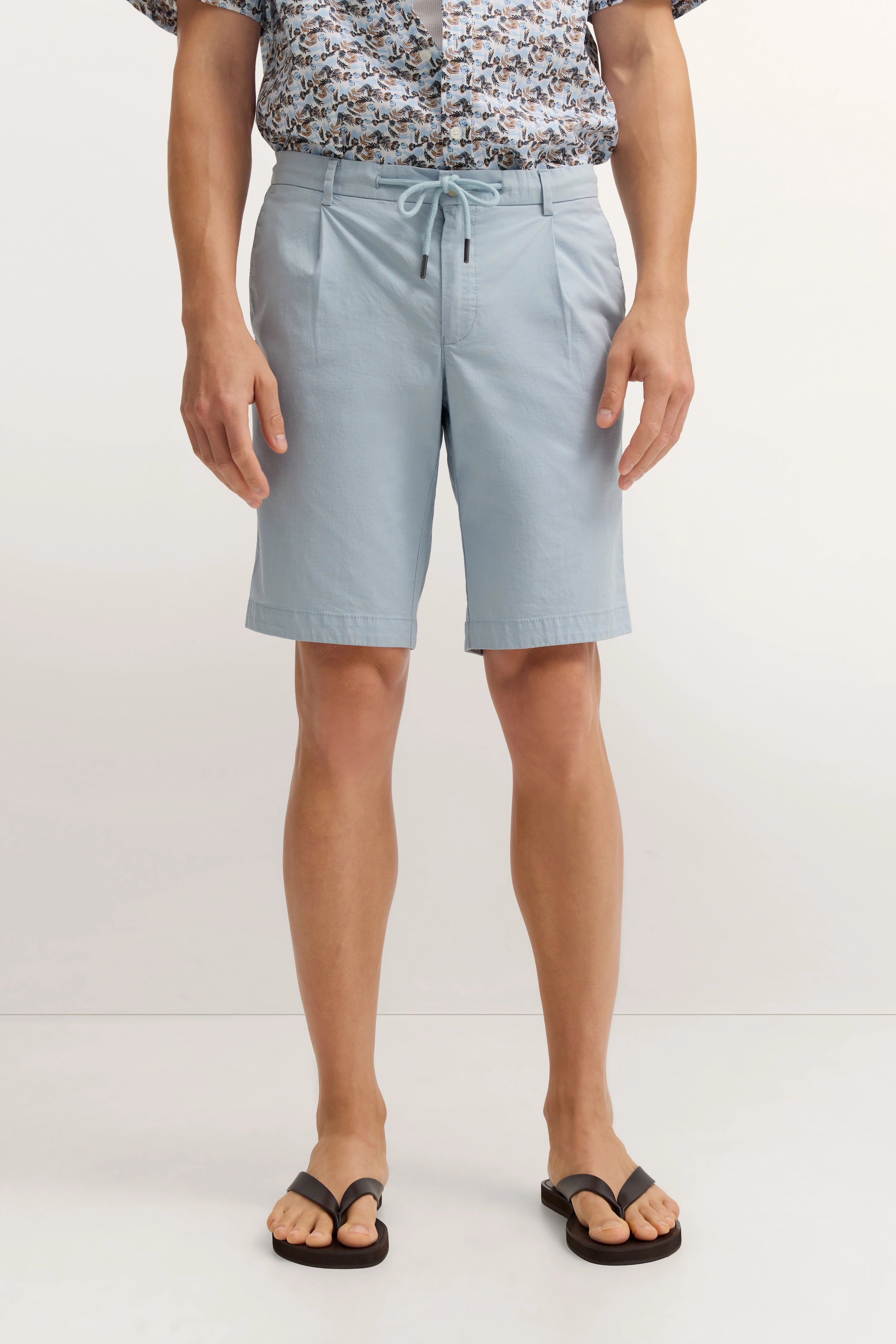 Hellblaue Shorts mit Kordelzug, florales Hemd, legeres Modelbild, entspannte Haltung.