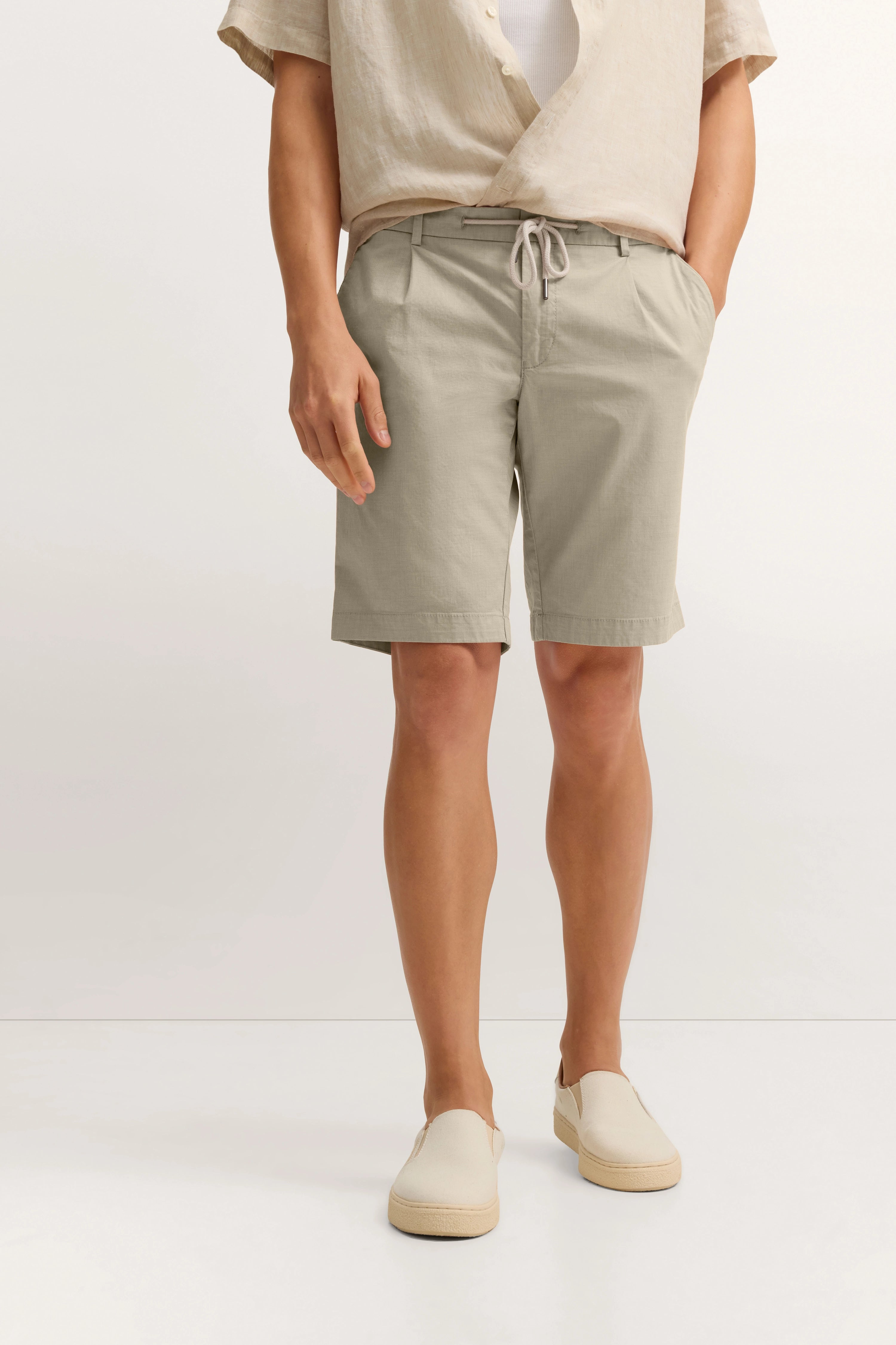 Beiges Freizeitoutfit mit Hemd und Shorts, legeres Modelbild, entspannte Pose, bugatti Stil.