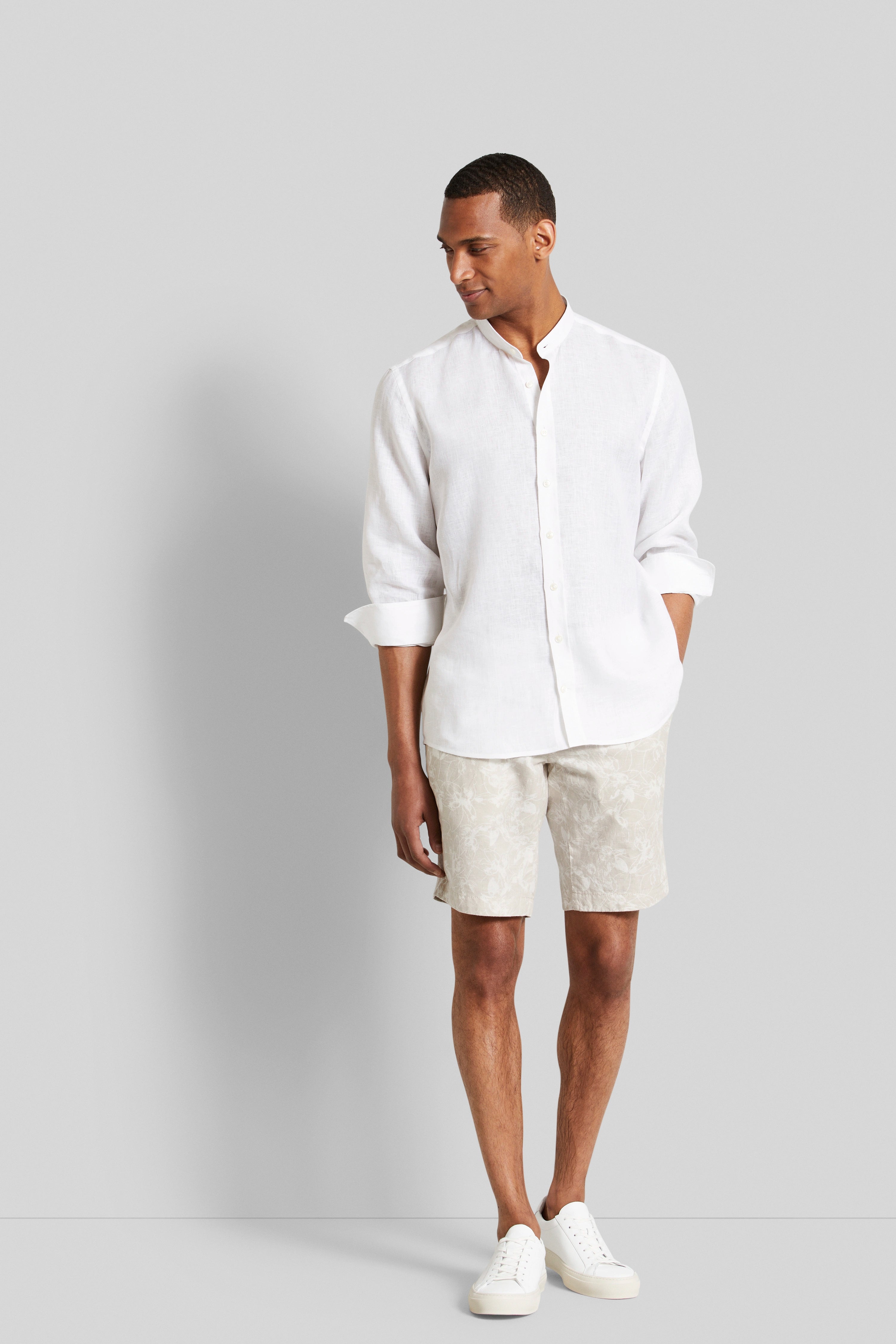 Model in weißem Leinenhemd und beigen gemusterten Shorts von bugatti, entspanntes Posing.