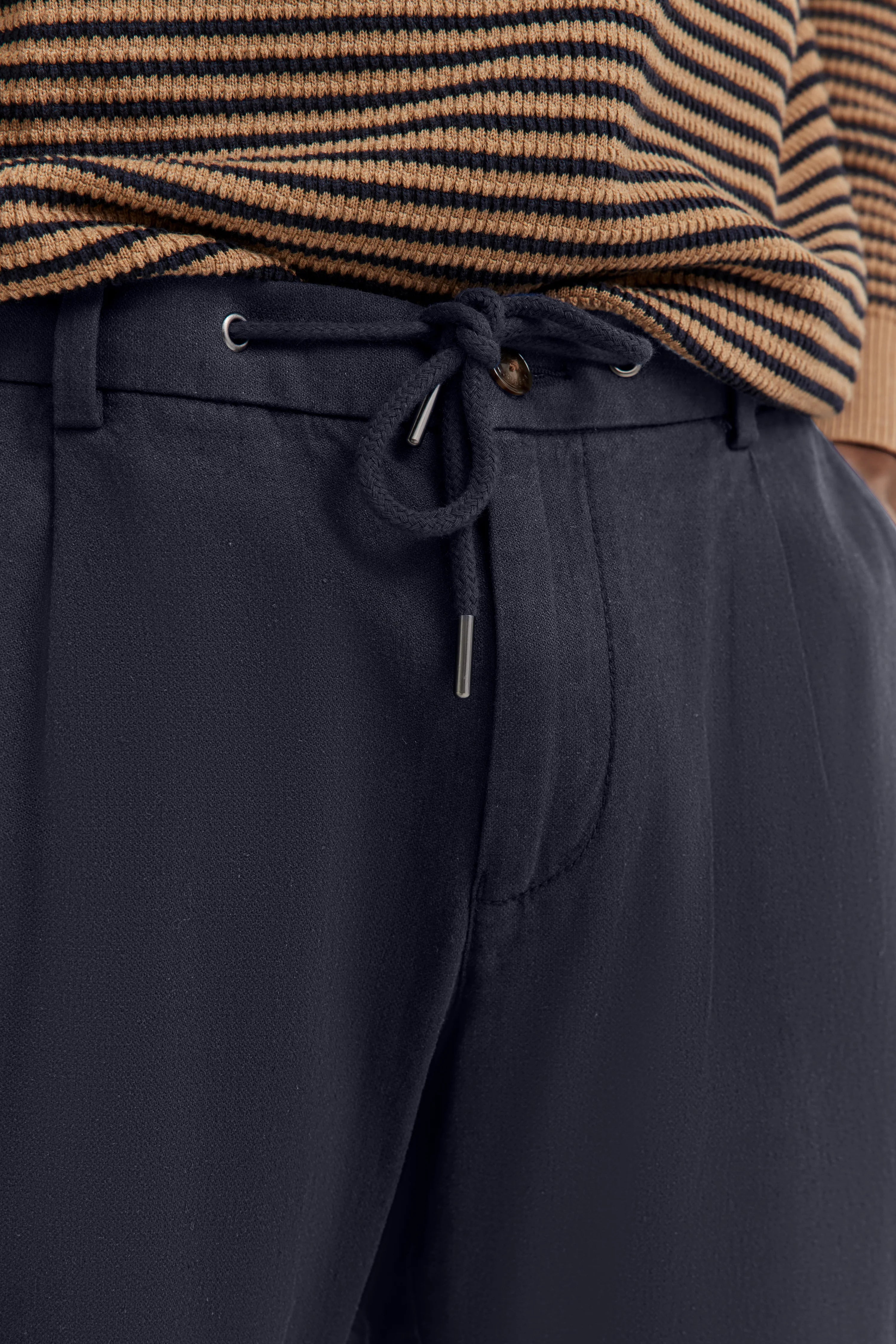 Dunkelblaue Hose mit Kordelzug und beige-schwarz gestreiftem Pullover, Detailansicht.