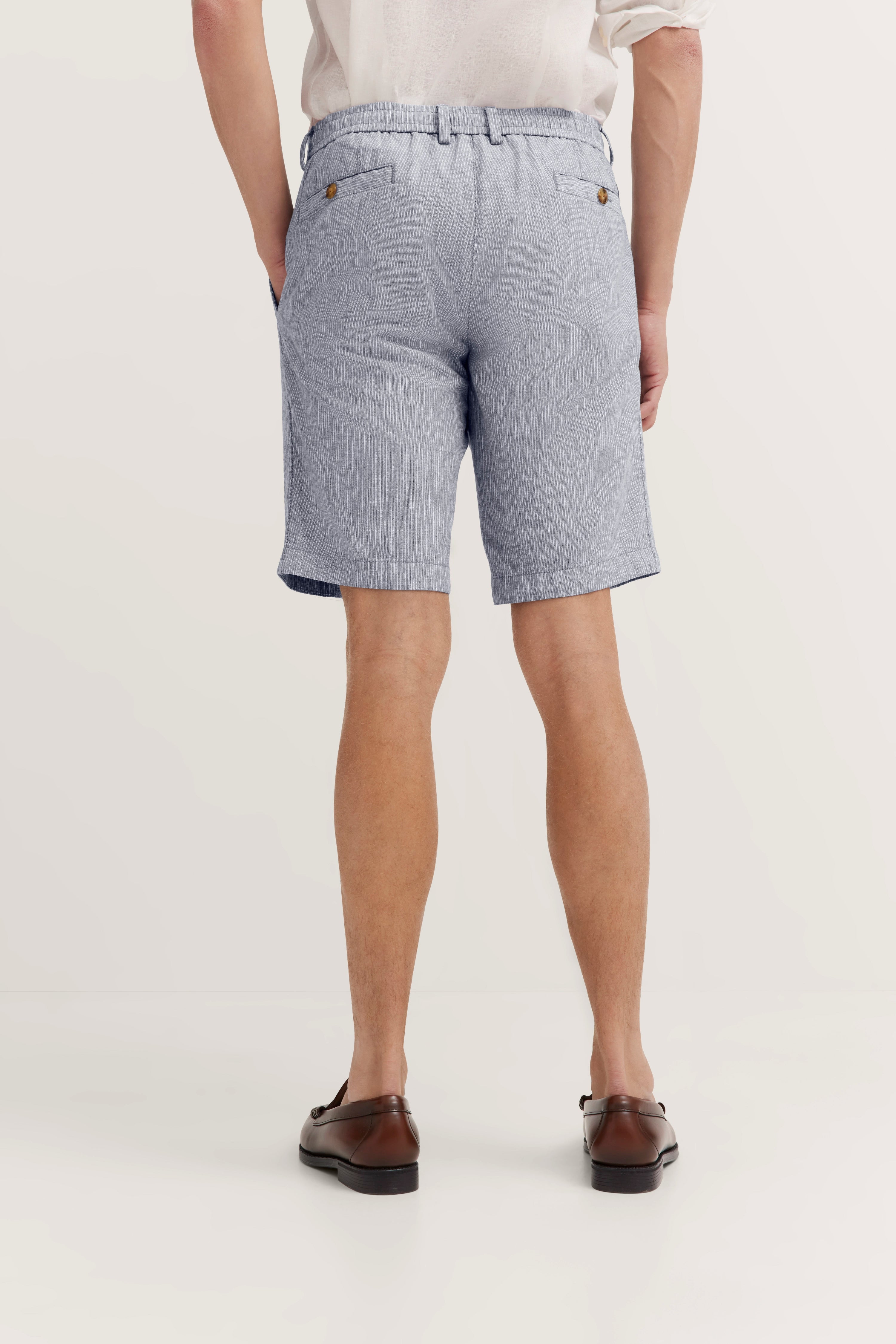 Herrenmodel in blauer Shorts und braunen Schuhen, Rückansicht, legeres Posing.