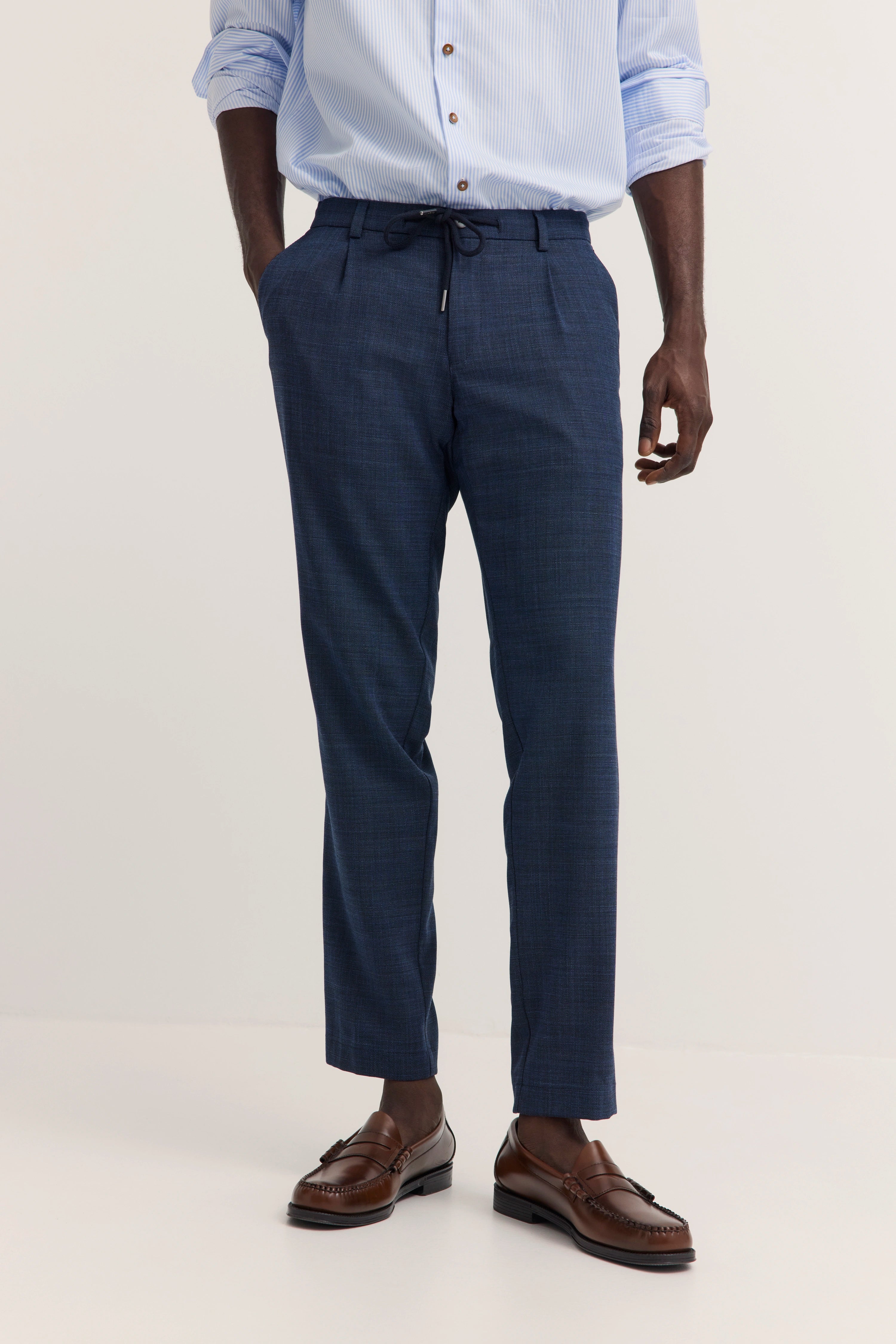 bugatti Modelbild: Blau-gestreifte Hemd, blaue Hose, braune Schuhe, entspannte Pose.