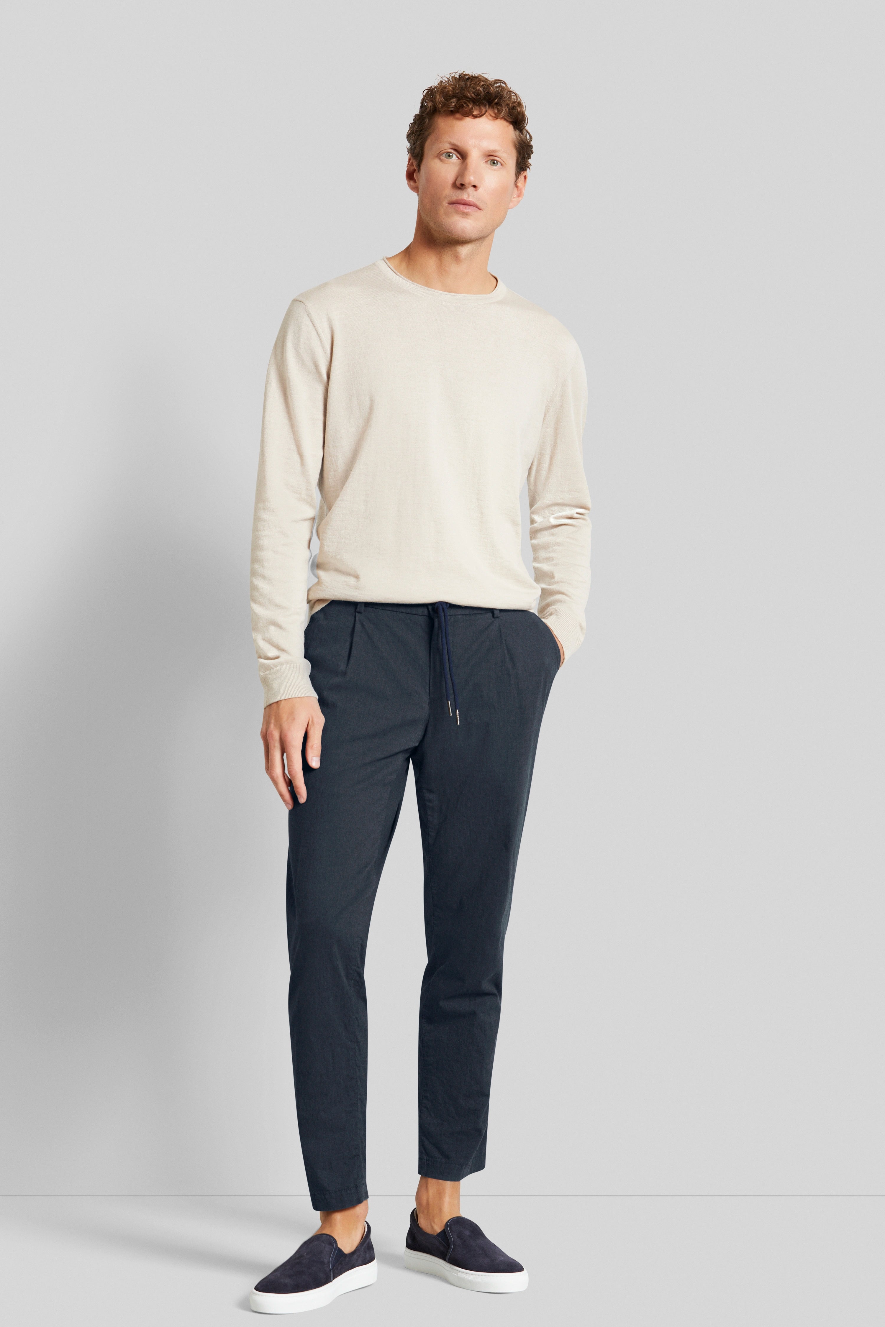 Beige longsleeve, donkerblauwe broek, donkerblauwe slip-ons, modelbeeld, ontspannen houding.