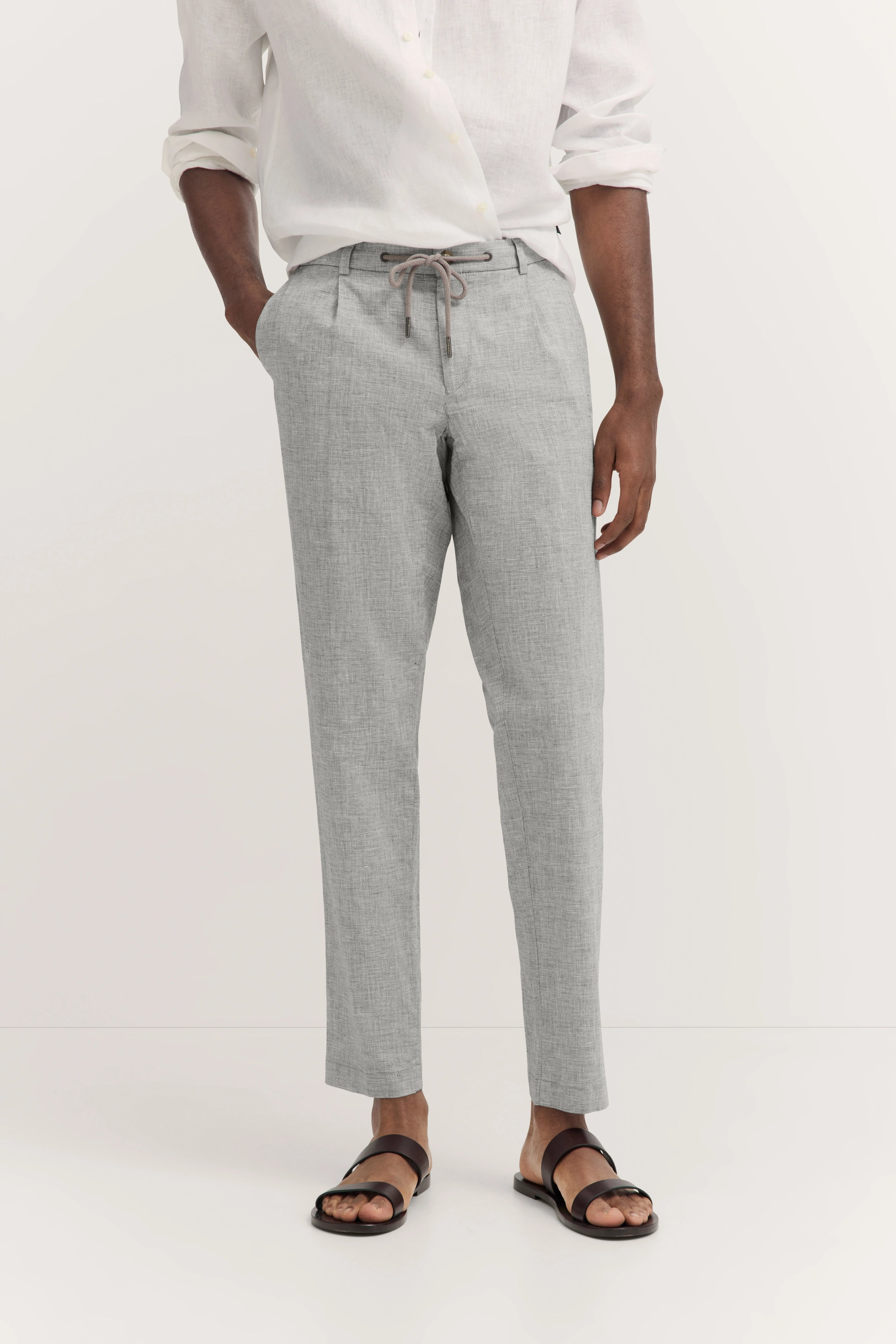 Wit shirt, grijze broek met patroon, bruine sandalen, casual modelfoto, ontspannen houding.