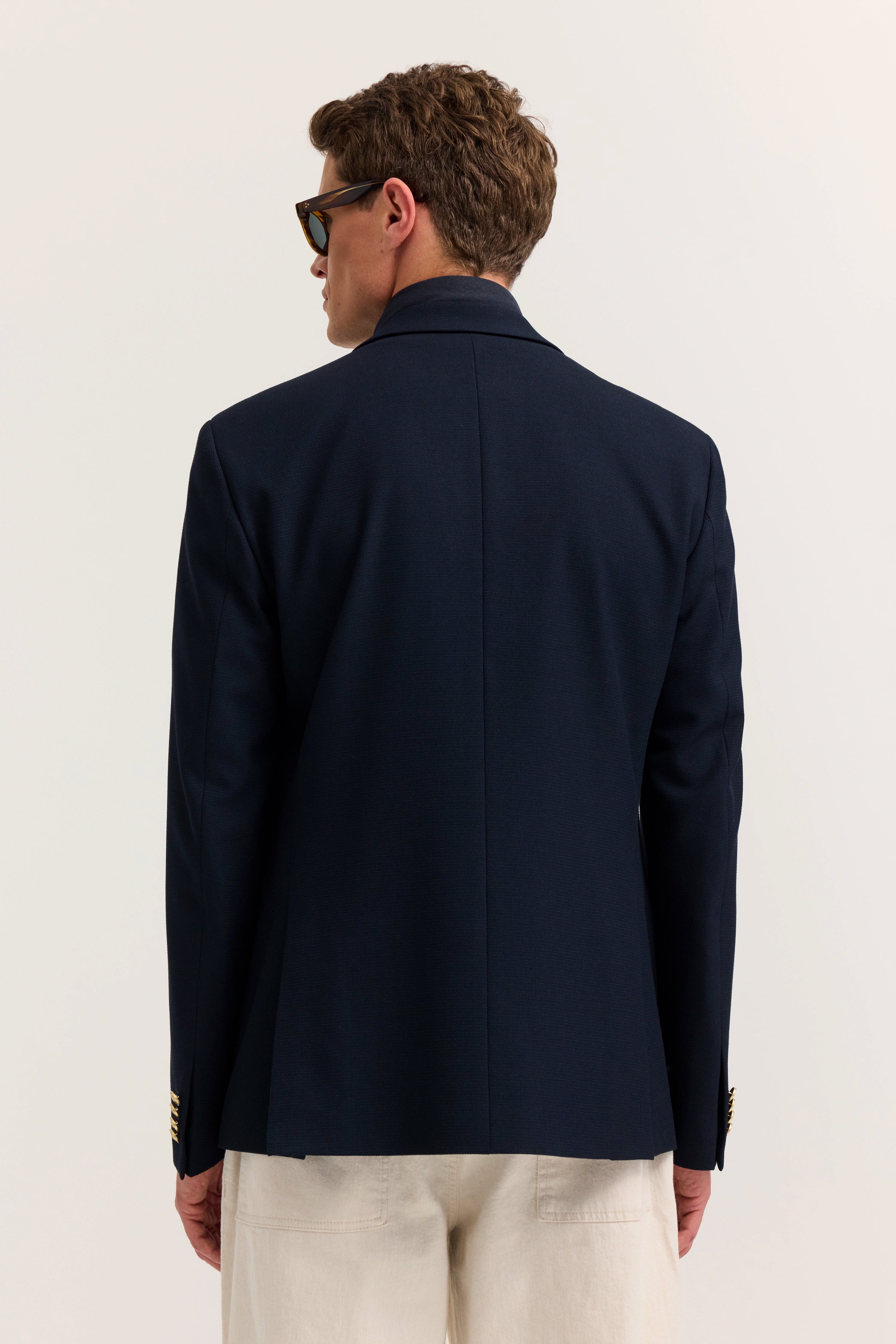 Navy Blazer und beige Hose von hinten, Modell steht entspannt mit Sonnenbrille.