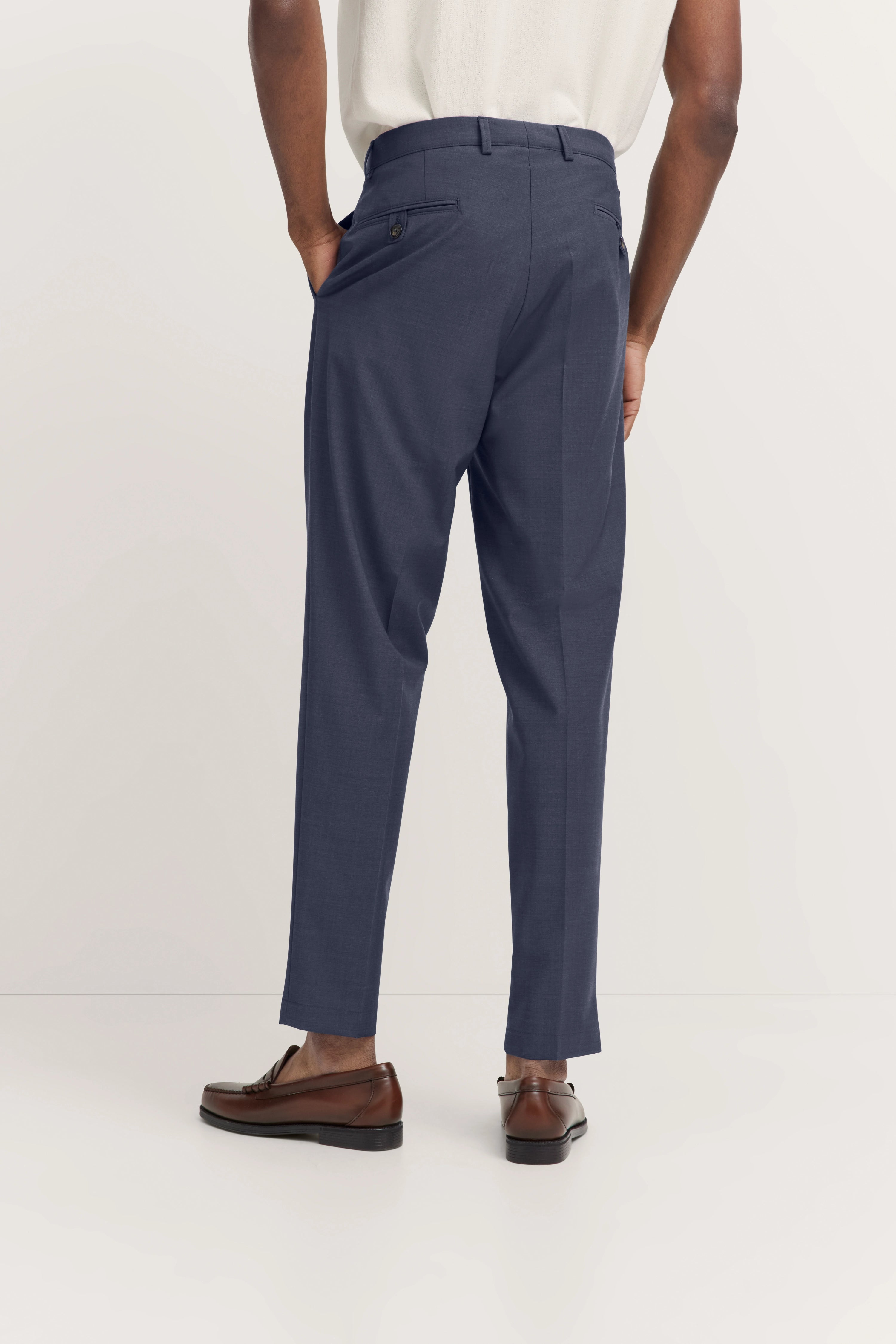 bugatti broek, donkerblauw, met wit overhemd. Model van achteren, ontspannen houding, bruine schoenen.