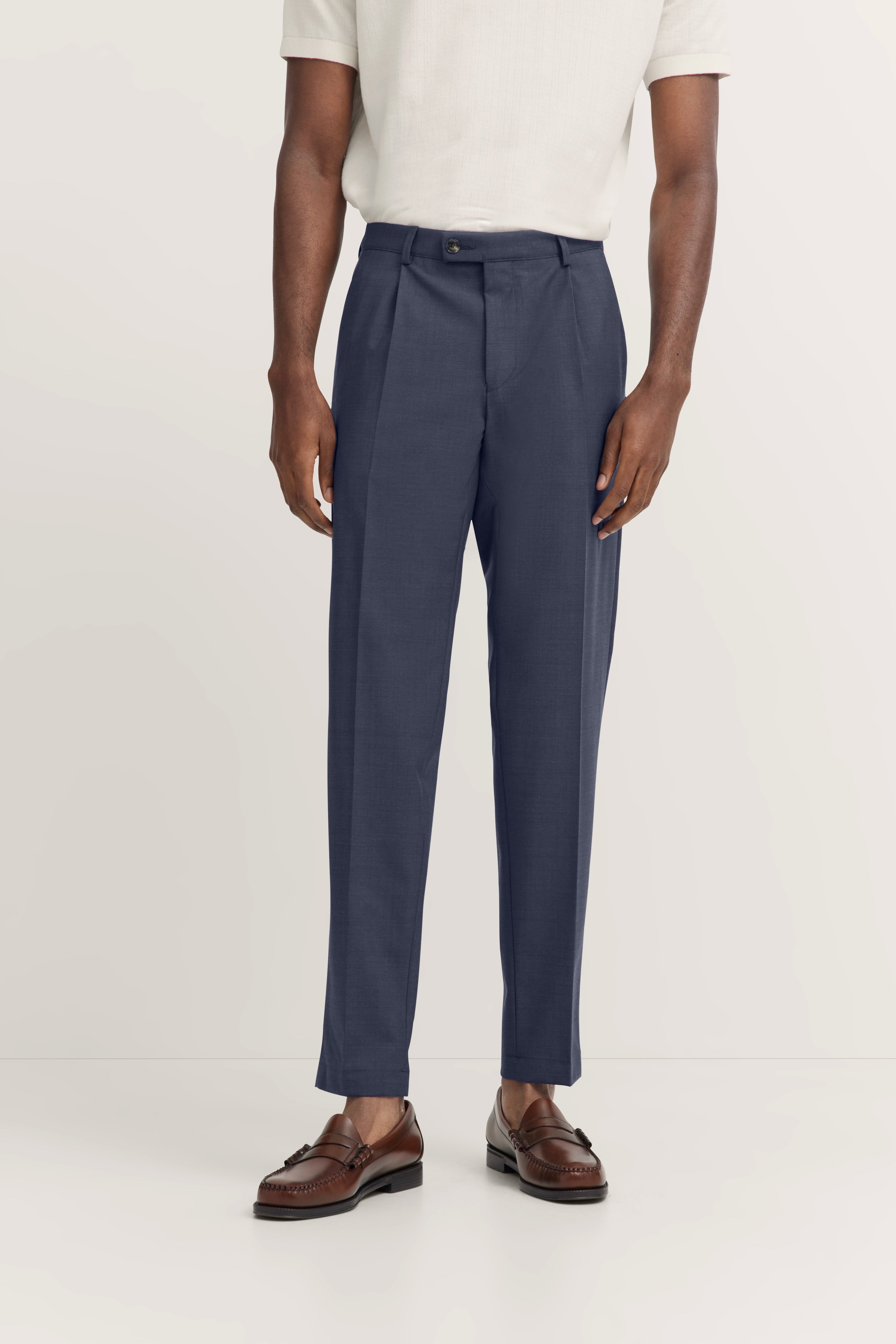 Donkerblauwe pantalon met wit overhemd, buste, elegante bruine loafers.