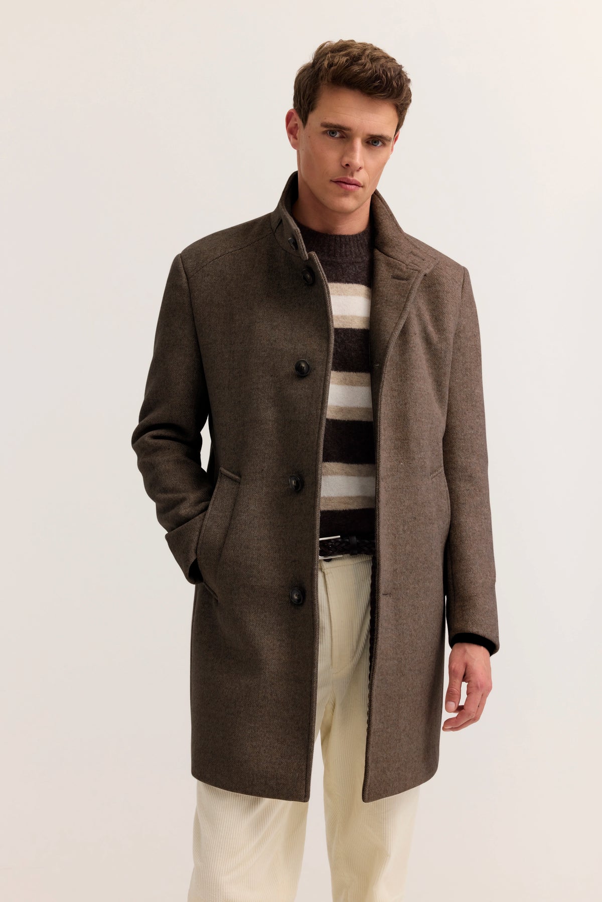 "bugatti Mantel braun, gestreifter Pullover, helle Hose, Modelbild, lässige Pose, zeitloser Stil."