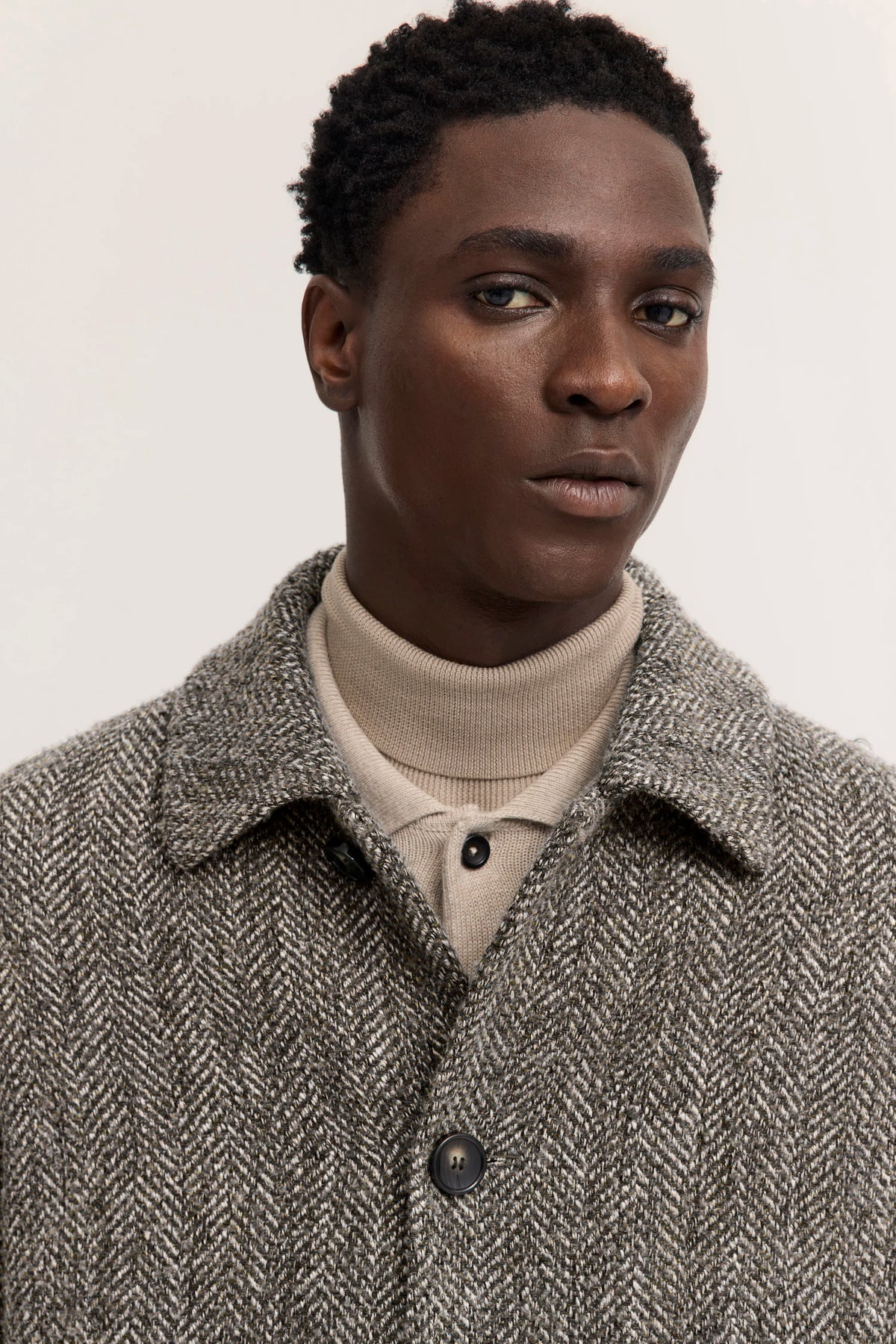 Model in grauem Tweed-Mantel, beige Hose und schwarzen Schuhen, von hinten, lässige Pose.