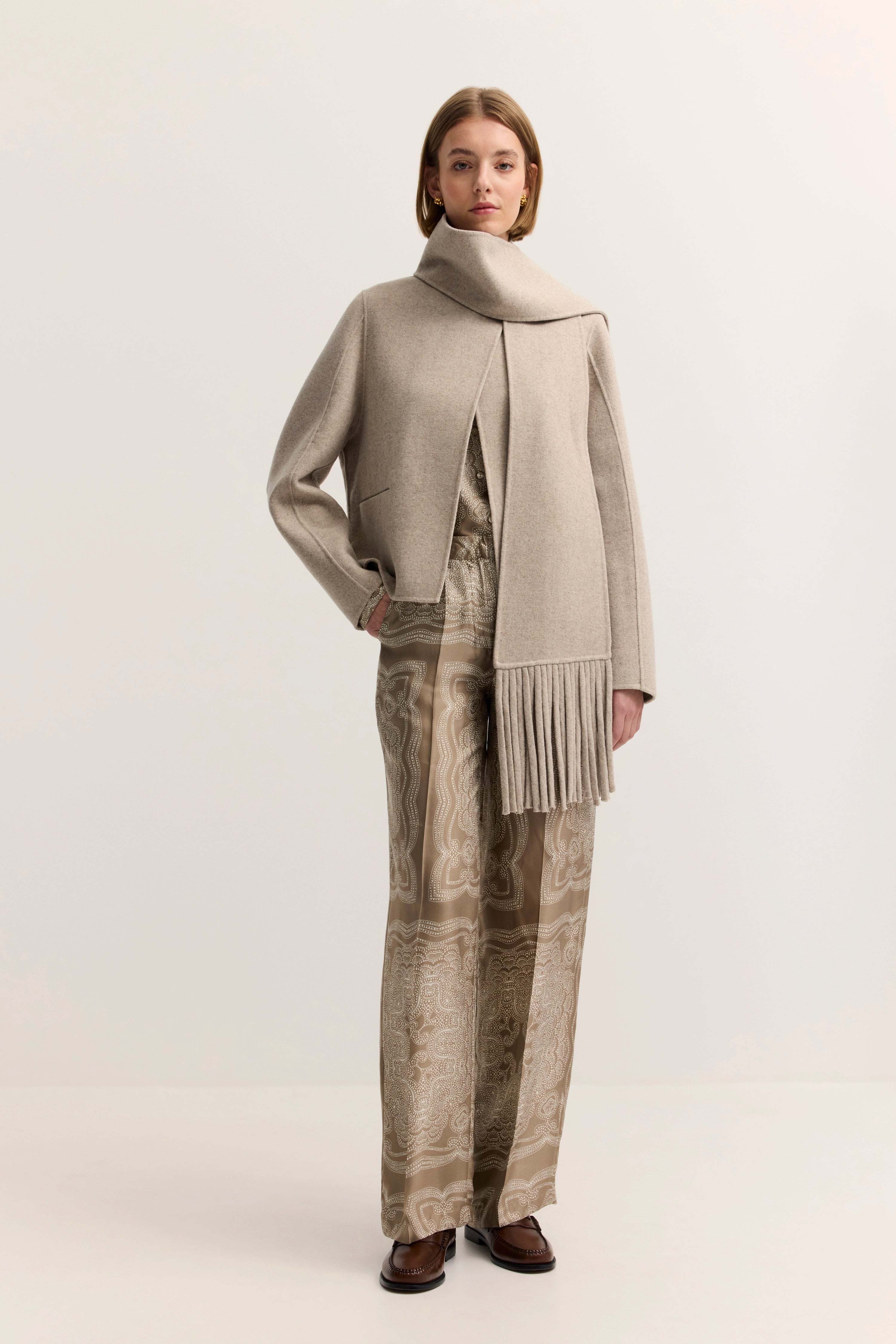 Elegante Modelaufnahme: Beiger bugatti-Mantel mit Schal, gemusterte Hose in Erdtönen, entspanntes Posing.