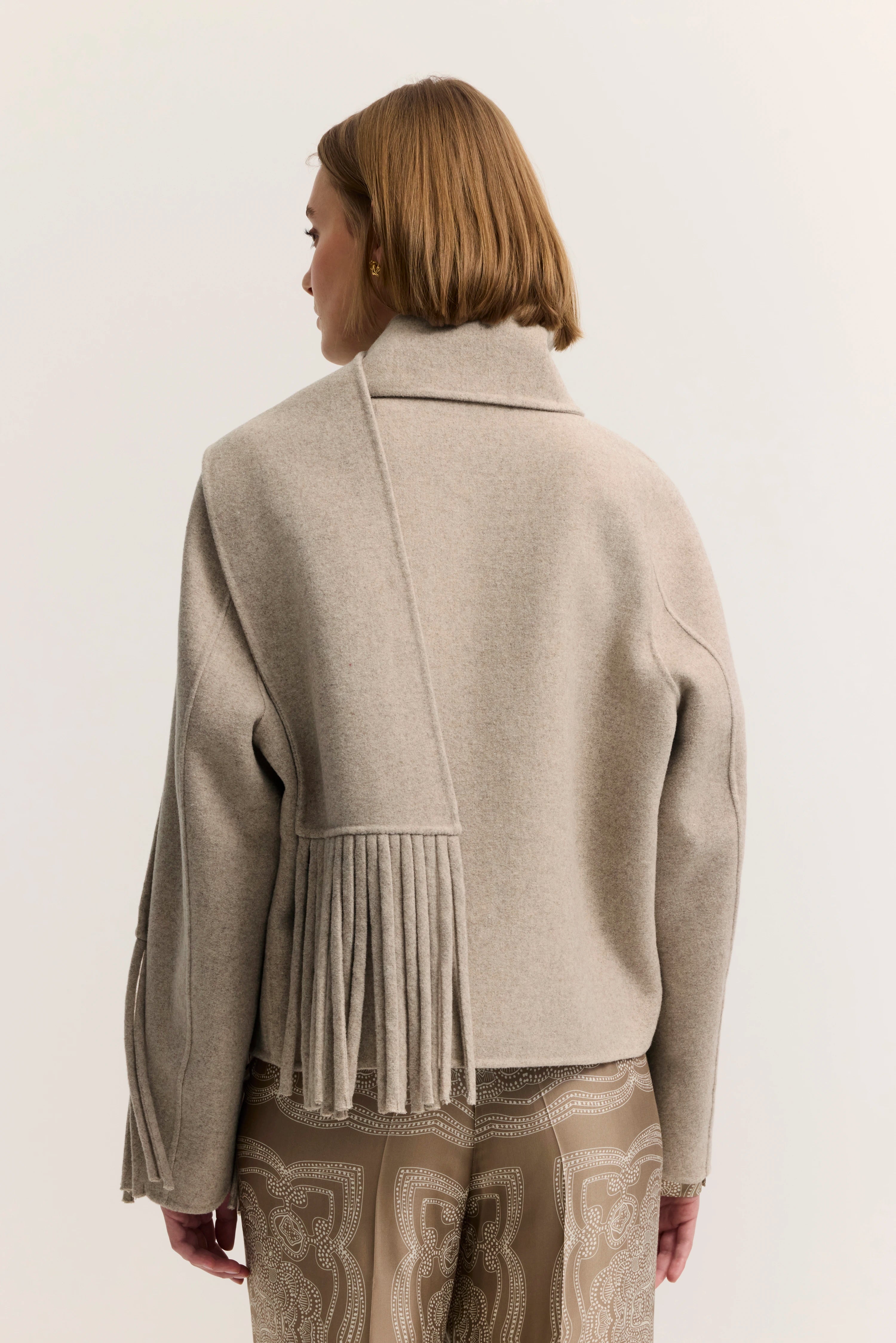 Beige Jacke mit Fransen und gemusterter Hose, Seitenansicht, legeres Modelbild.