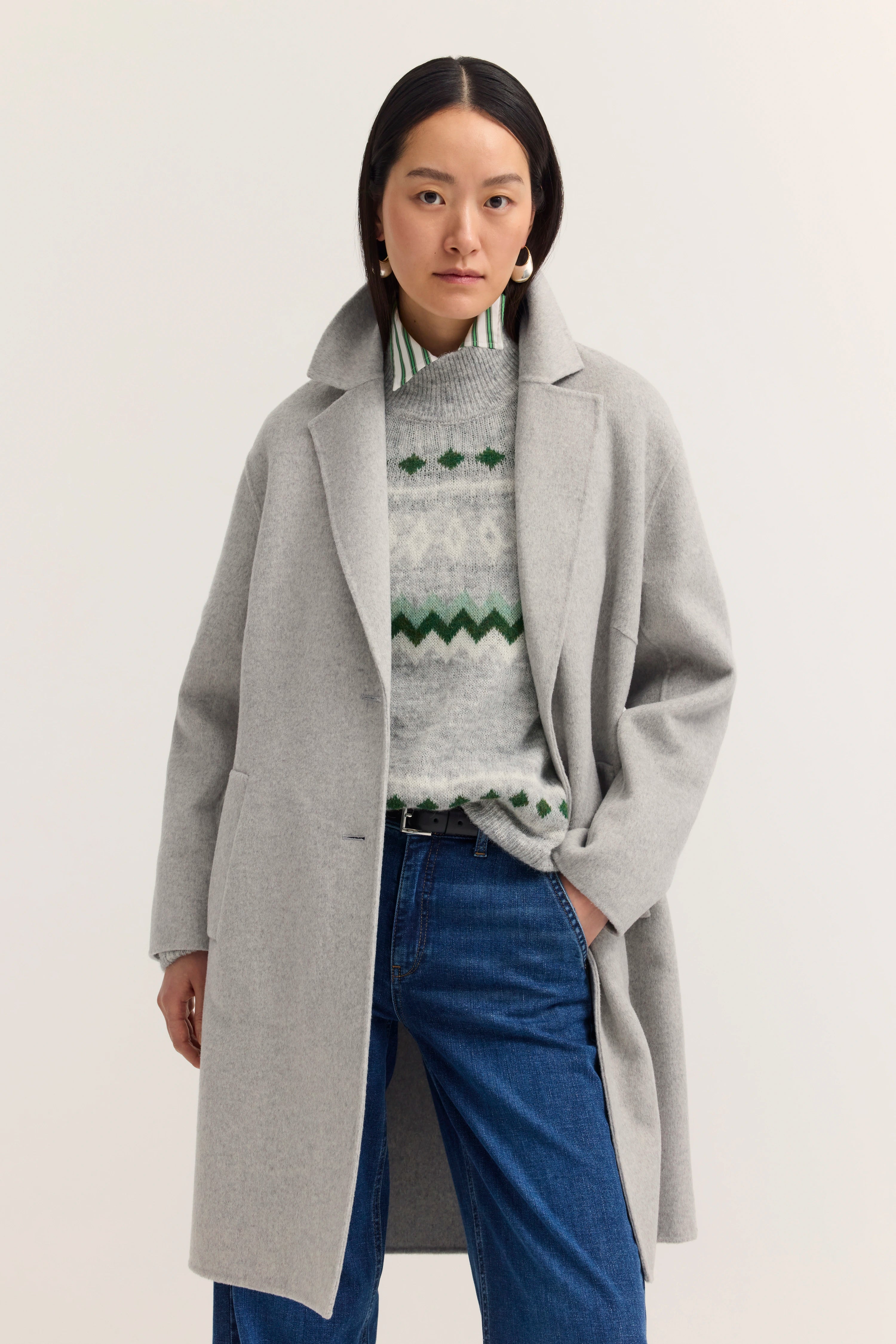 Grauer Mantel, gemusterter Pullover in Grau-Grün, blaue Jeans
