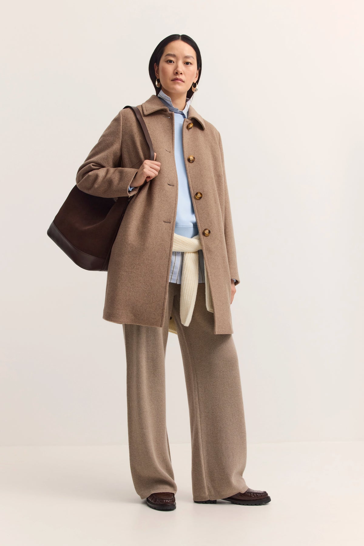 Model in beigem Mantel, blauer Bluse, beiger Hose