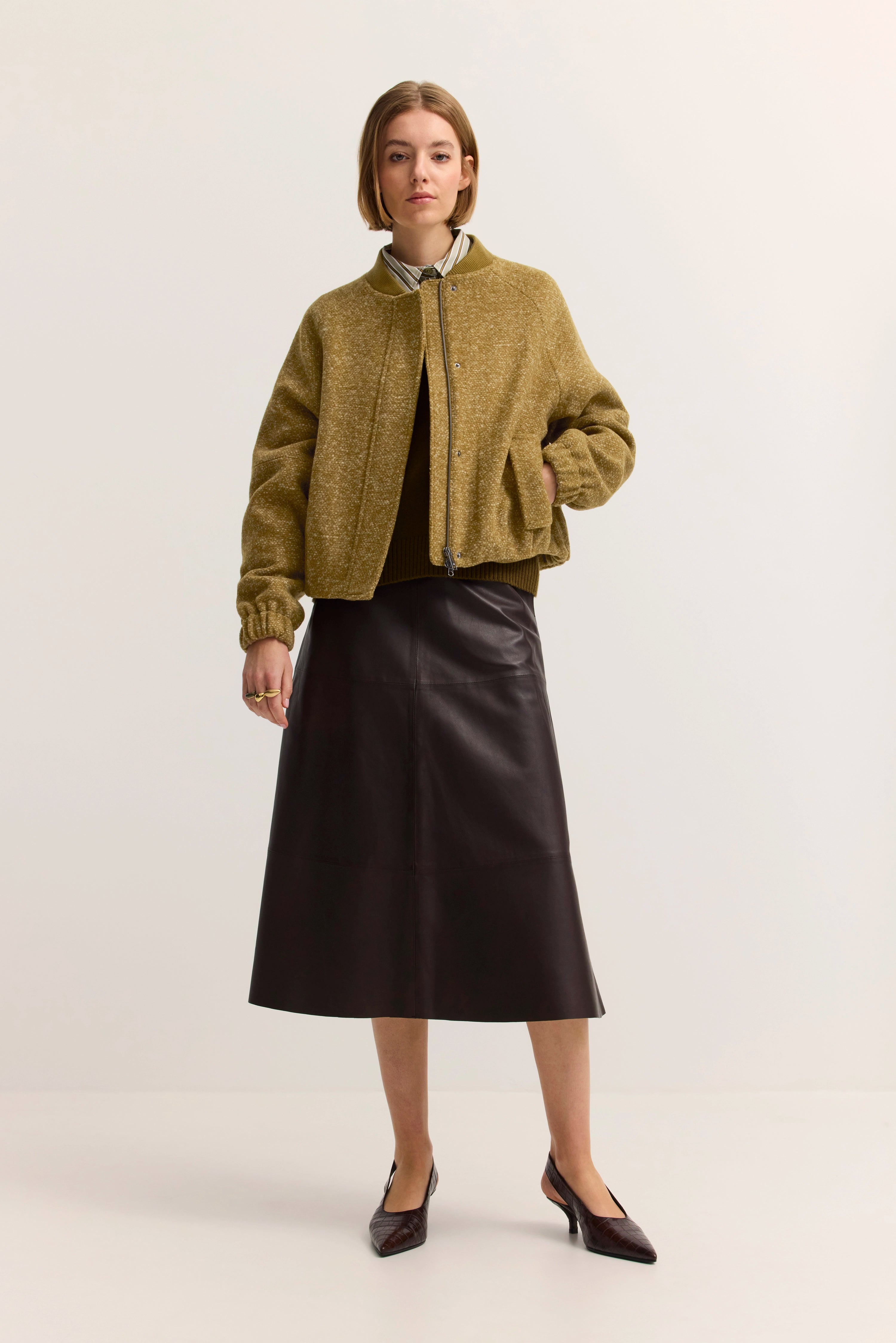 Model trägt olivgrüne Jacke, braunen Rock und Hemd