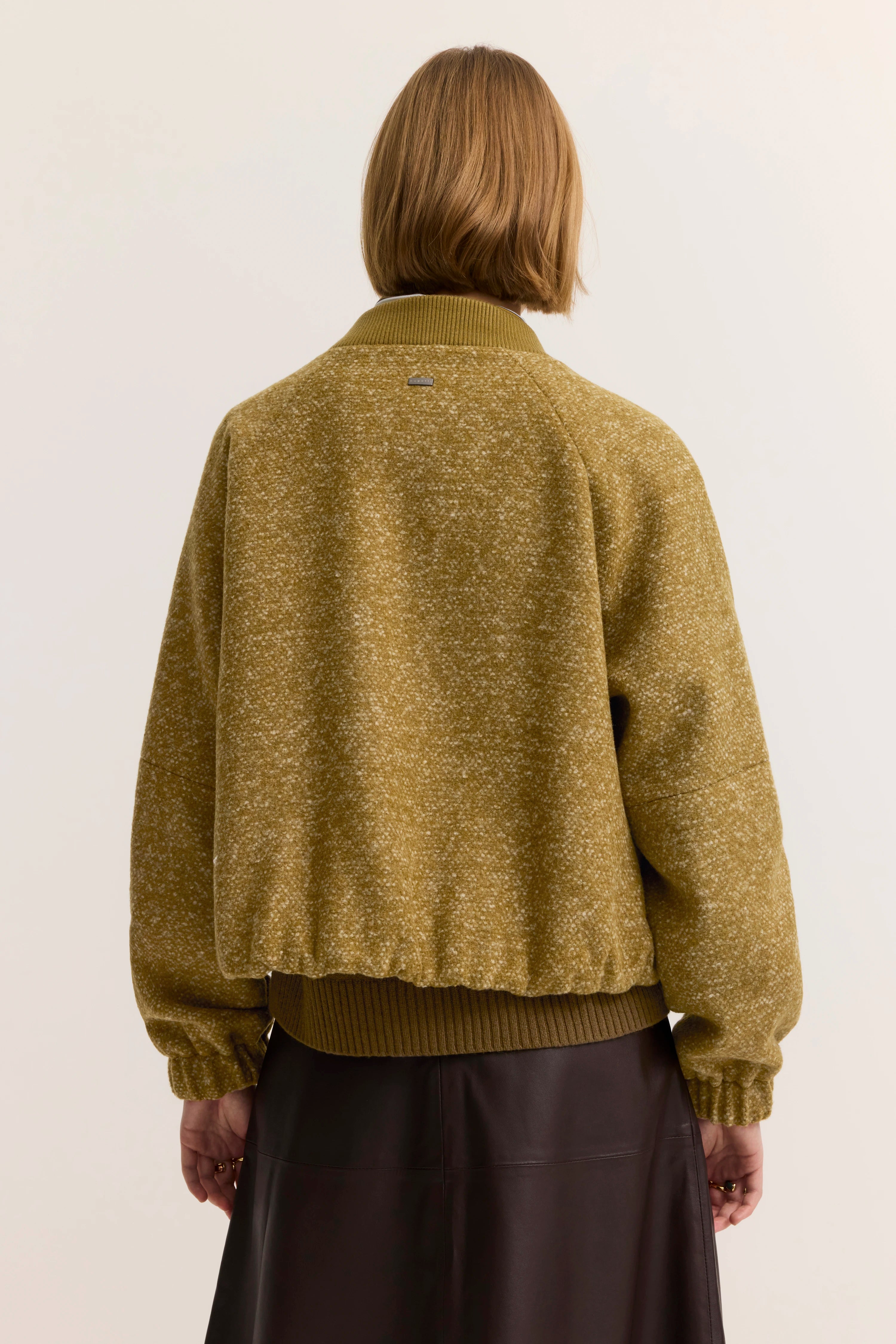 Rückansicht eines Models in olivgrüner bugatti Jacke mit Muster, kombiniert mit schwarzem Rock.