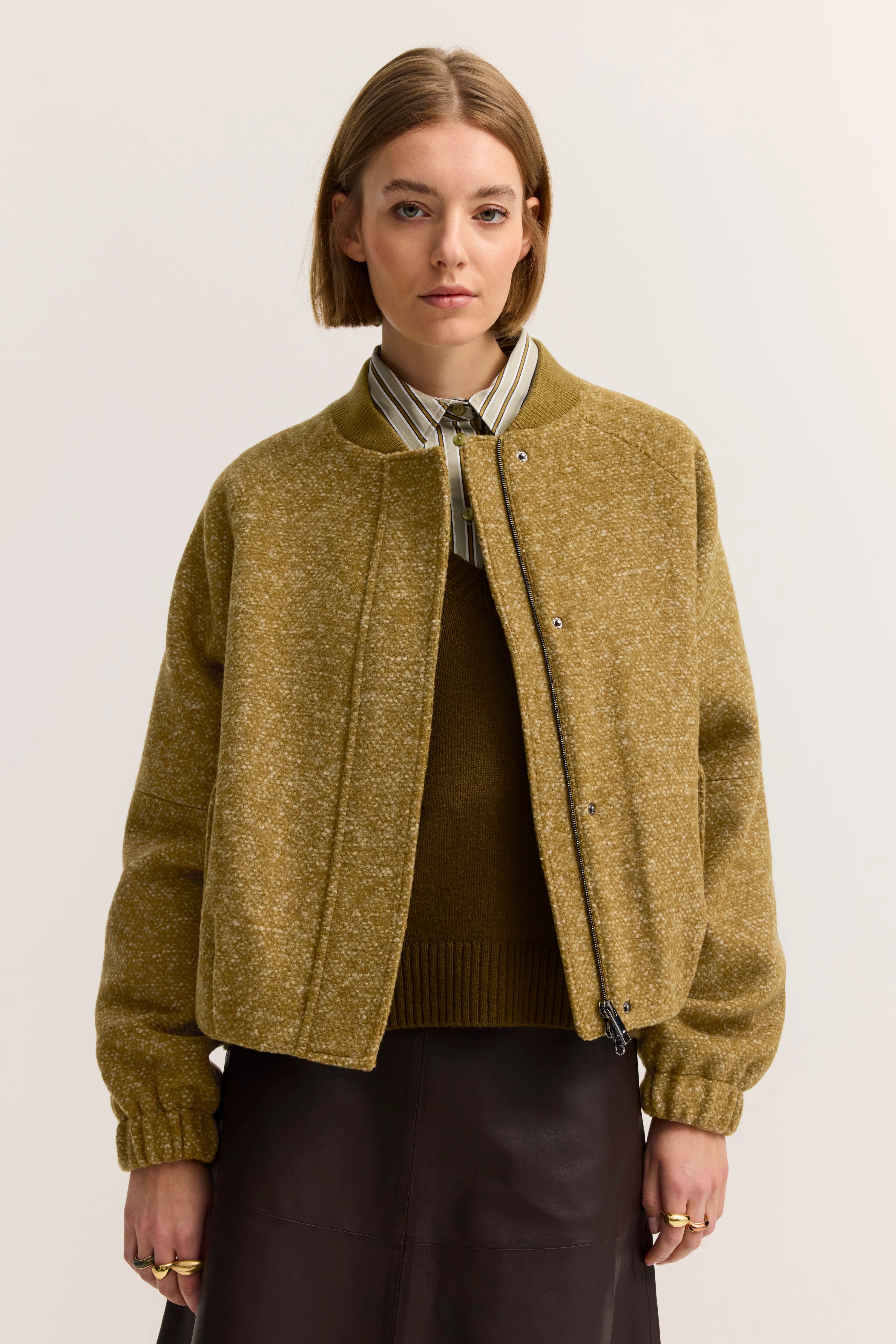 Model in olivgrüner bugatti Jacke, gestreiftes Hemd, legeres Posing, zeitloser Stil.