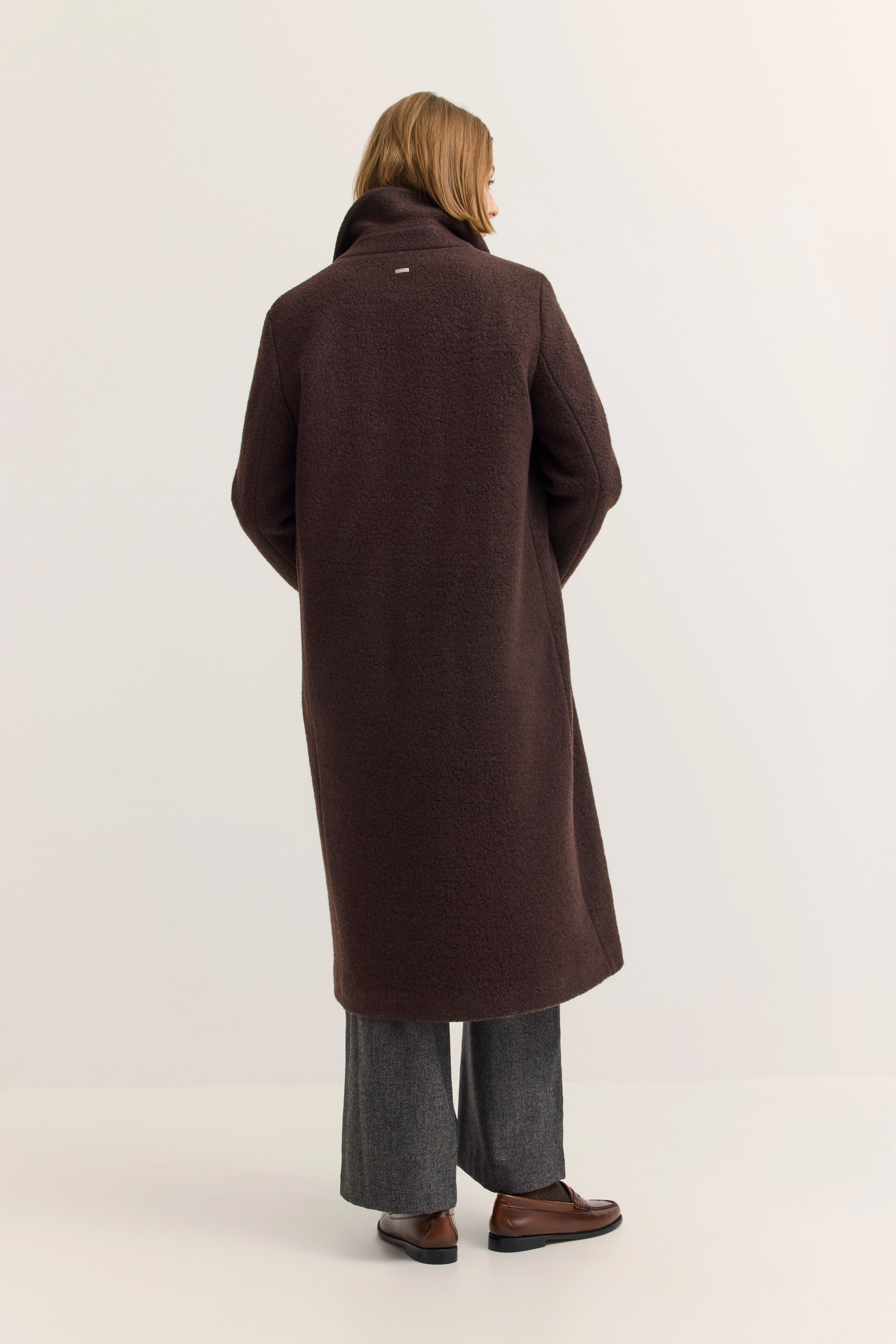 Model in braunem bugatti Mantel, Rückenansicht, graue Hose, braune Schuhe, entspanntes Posing.