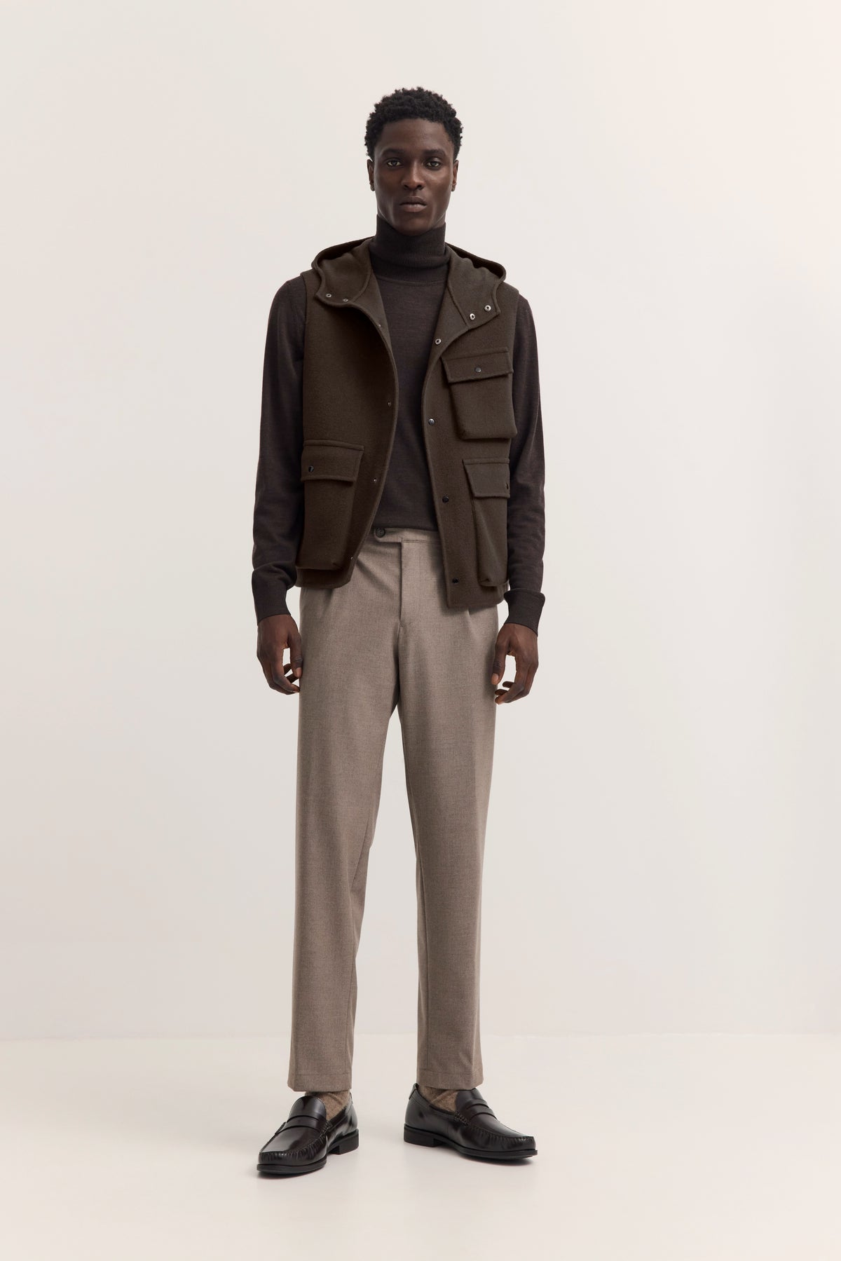Brauner bugatti Wollmantel mit Kapuze, schwarzer Rollkragenpullover, Model im Profil.