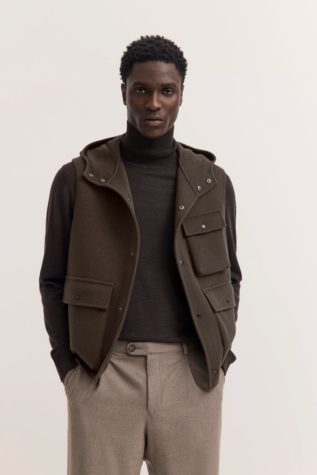 Model in braunem Rollkragenpullover, olivgrüner Weste und beige Hose