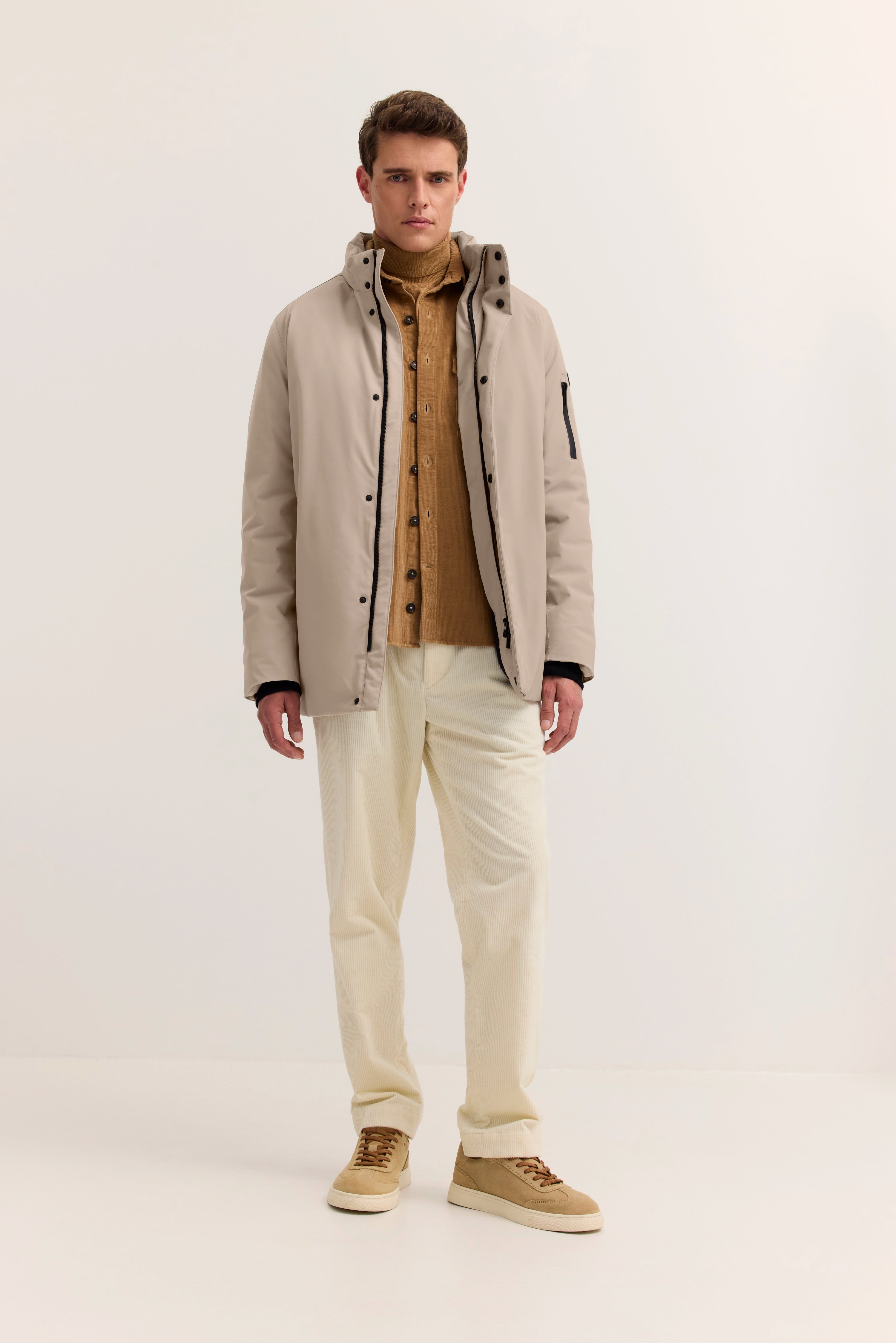 Beigefarbene Jacke, brauner Rollkragen, cremefarbene Hose, Model steht gerade.