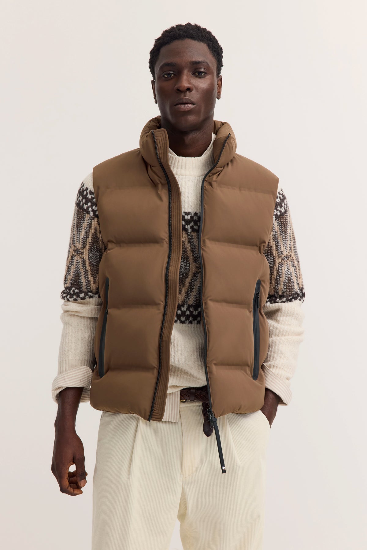 Braune Steppweste über cremefarbenem Pullover mit Muster, Modelbild, lässige Pose.