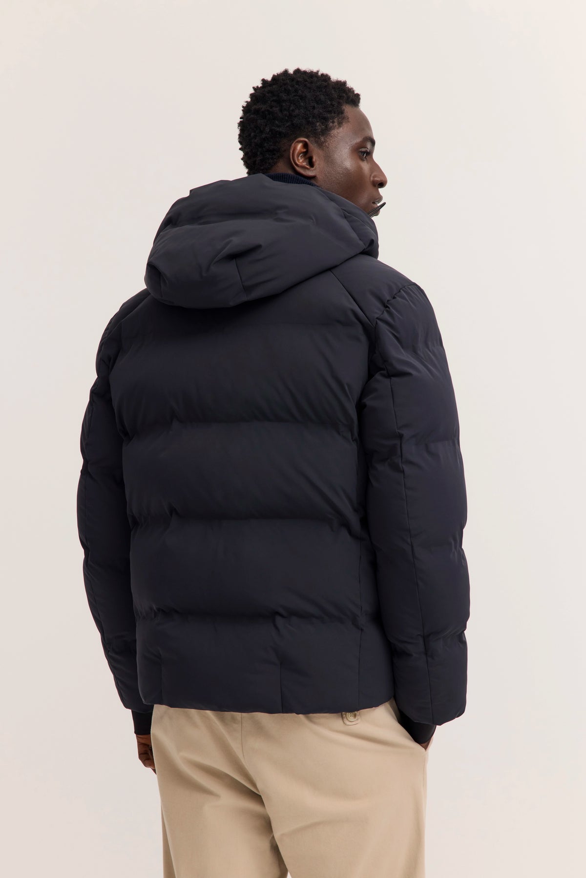 Schwarze bugatti Daunenjacke, beige Hose, Model von hinten, lässige Haltung.