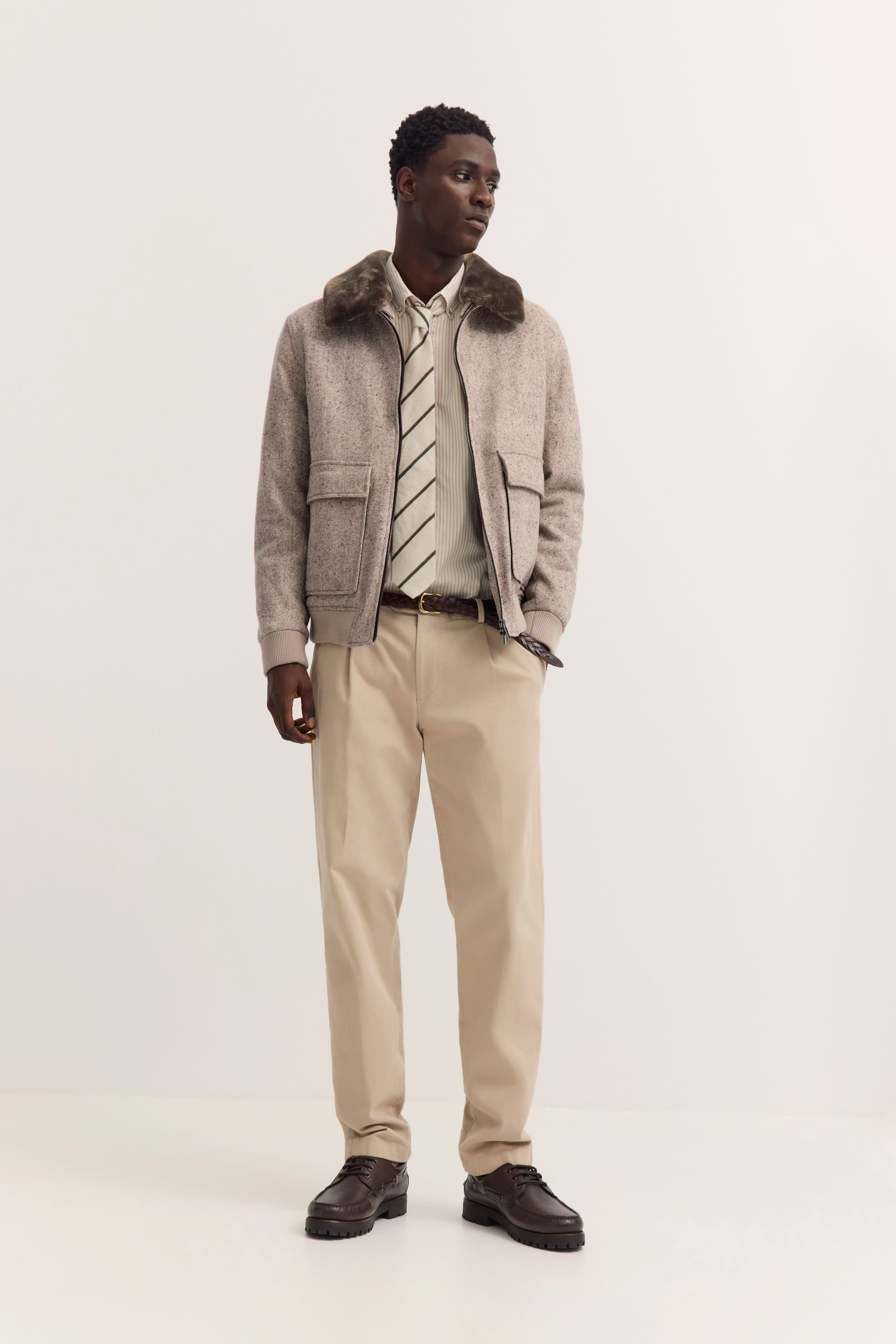 Model in beigem bugatti-Outfit: Jacke mit Fellkragen, gestreiftem Hemd, Krawatte, Chinos und braunen Schuhen.