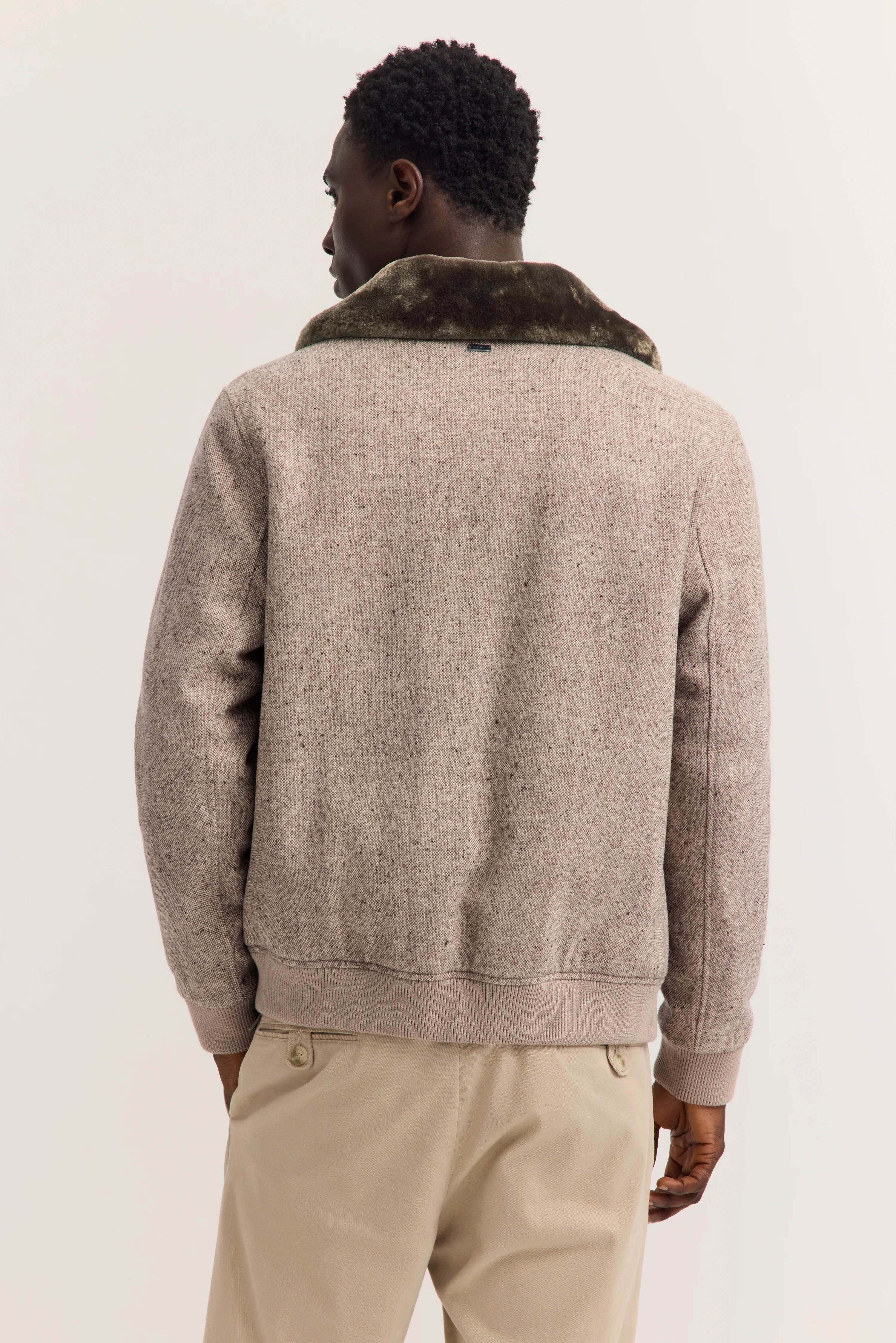 Herrenmodel von hinten in beiger bugatti-Jacke mit Kunstfellkragen, beige Hose.