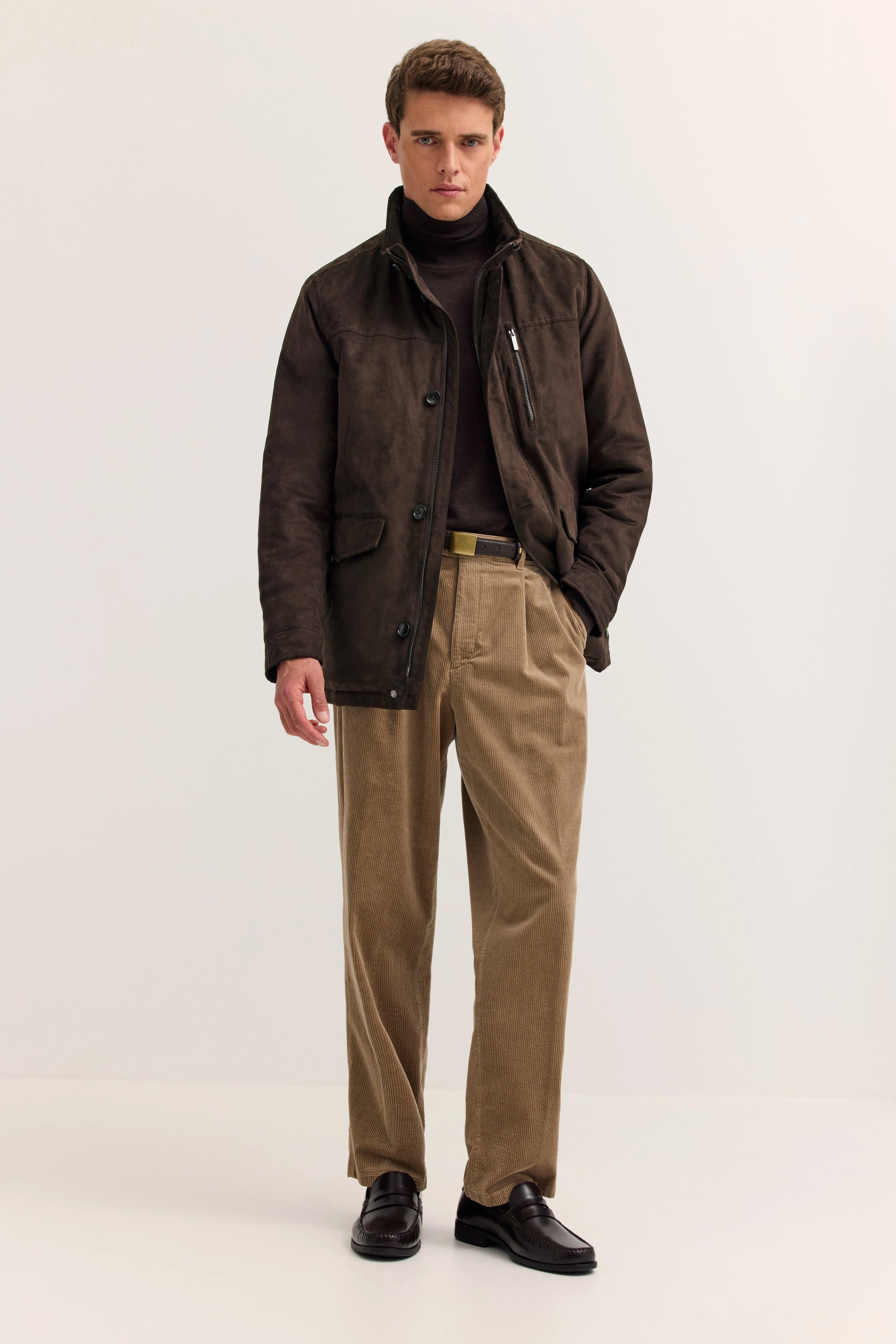 Model in brauner bugatti-Jacke, Rollkragenpullover, beige Cordhose, schwarze Schuhe. Stehpose.