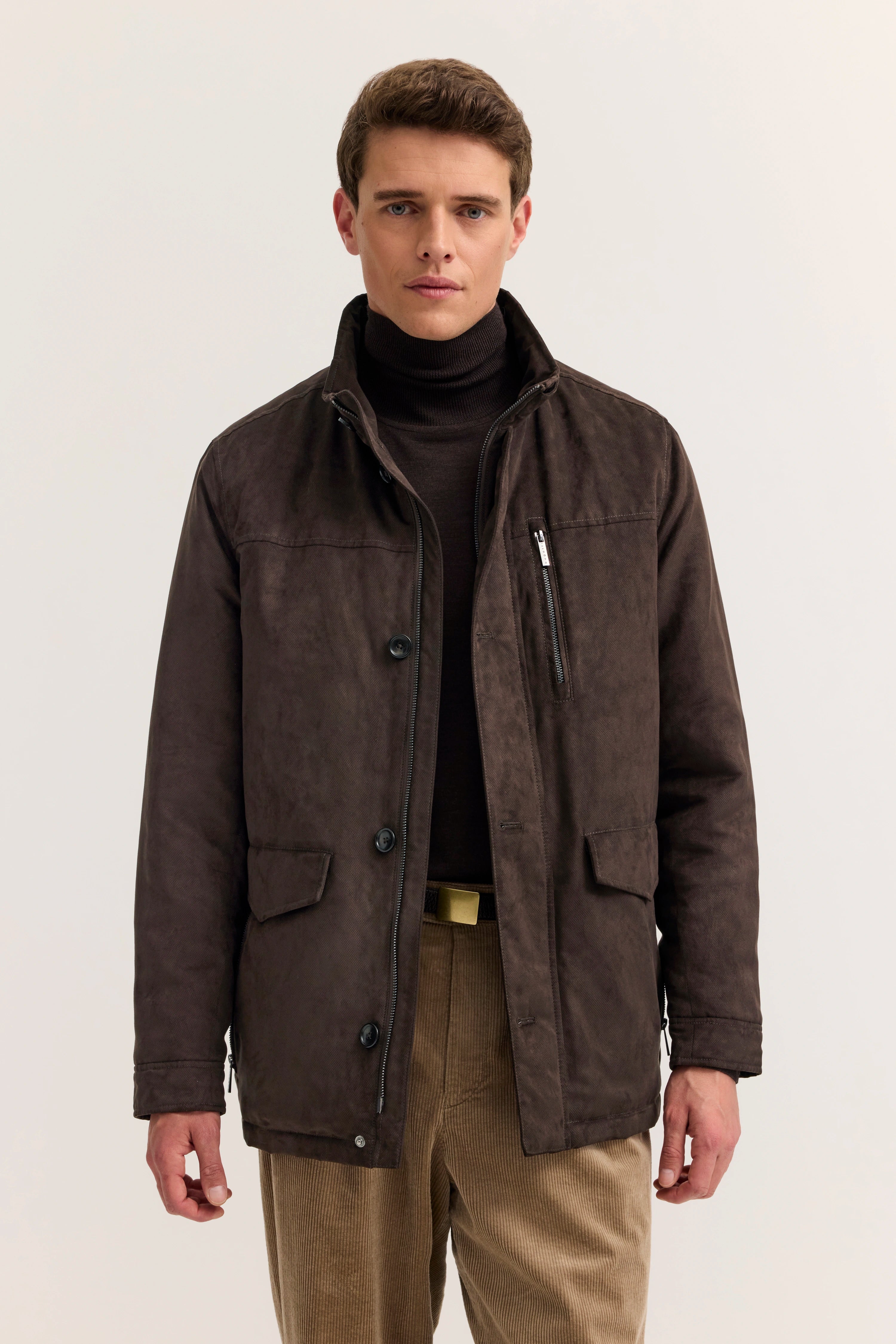 Model in brauner bugatti Jacke, schwarzer Rollkragen, beige Cordhose, frontal, entspannte Haltung.