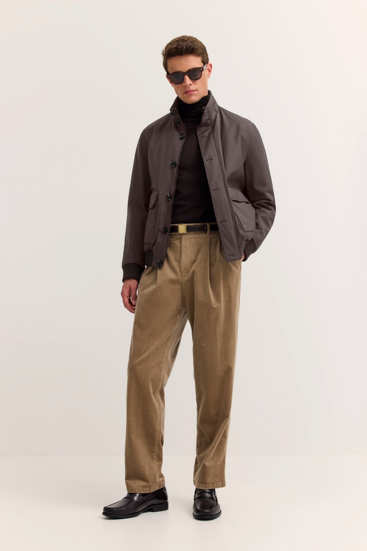 Model in brauner bugatti-Jacke, schwarzem Rollkragen und beigen Cordhosen. Lässig mit Händen in Taschen.